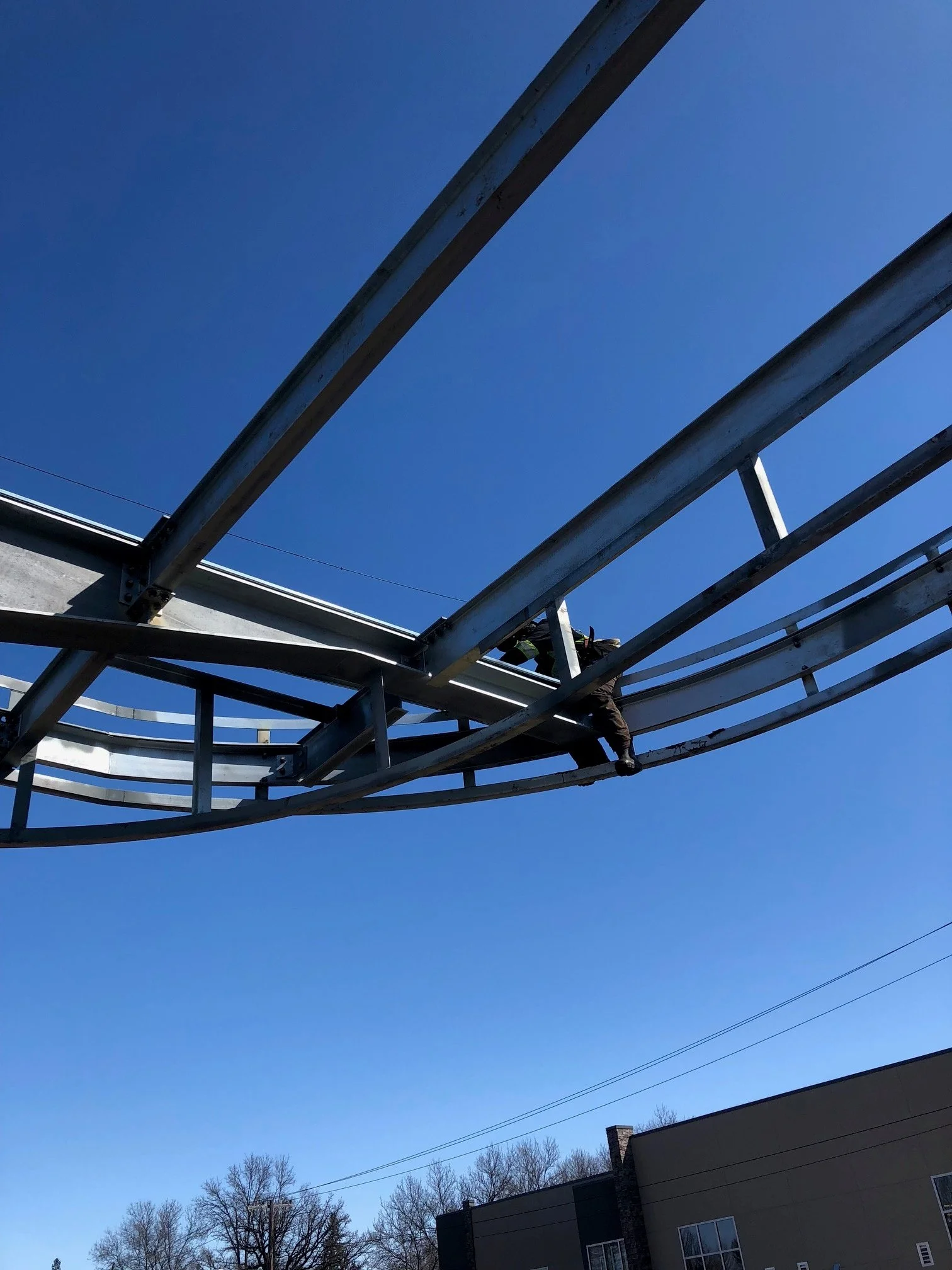 A construction worker is climbing on steel framework of a roller coaster track against a clear blue sky.