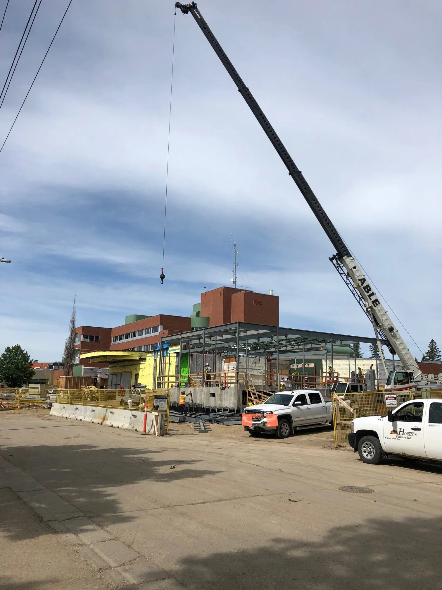 Construction site with a crane lifting materials, workers assembling a building frame, and a multi-story building in the background.