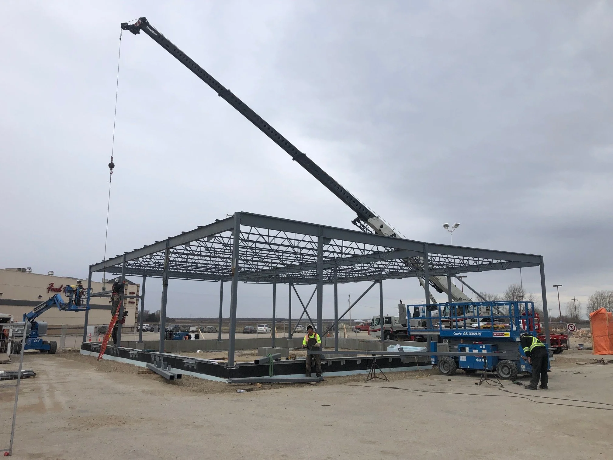 Construction site with steel framework structure, crane lifting components, and workers assembling the building.