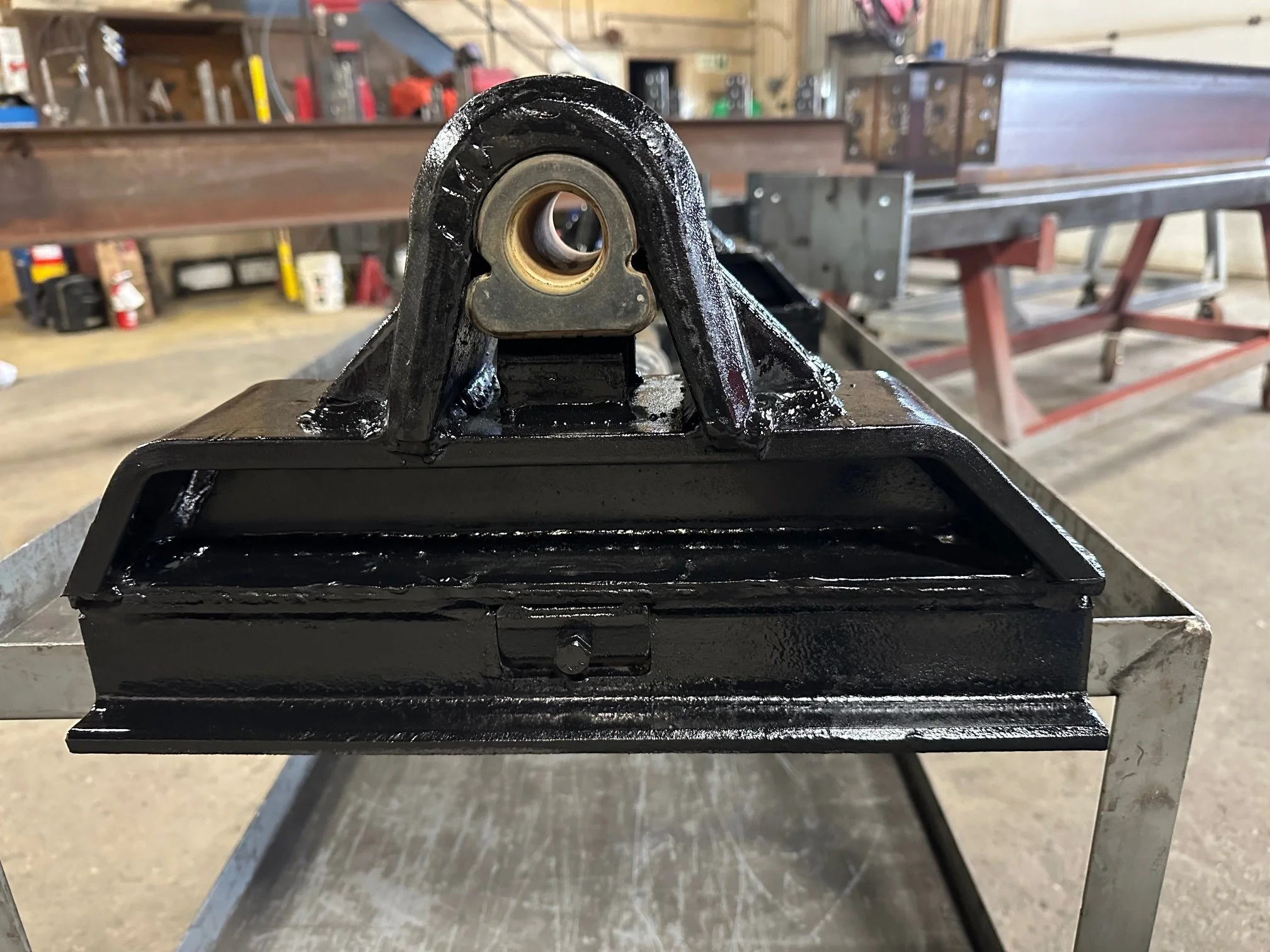Close-up of a black painted metal mechanical part with a bearing in a workshop with tools and equipment in the background.
