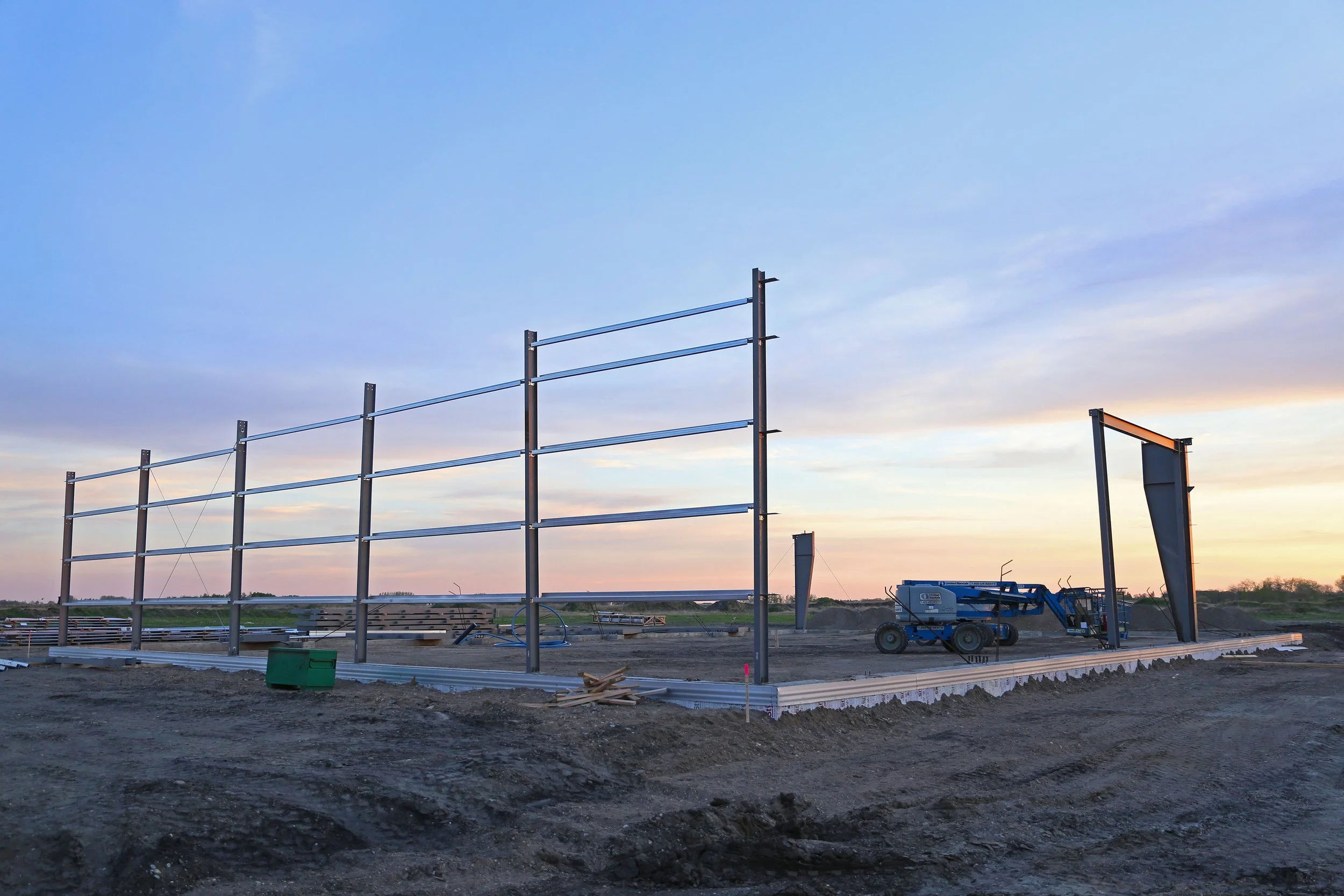 Steel framework for a building under construction on a dirt lot at sunset