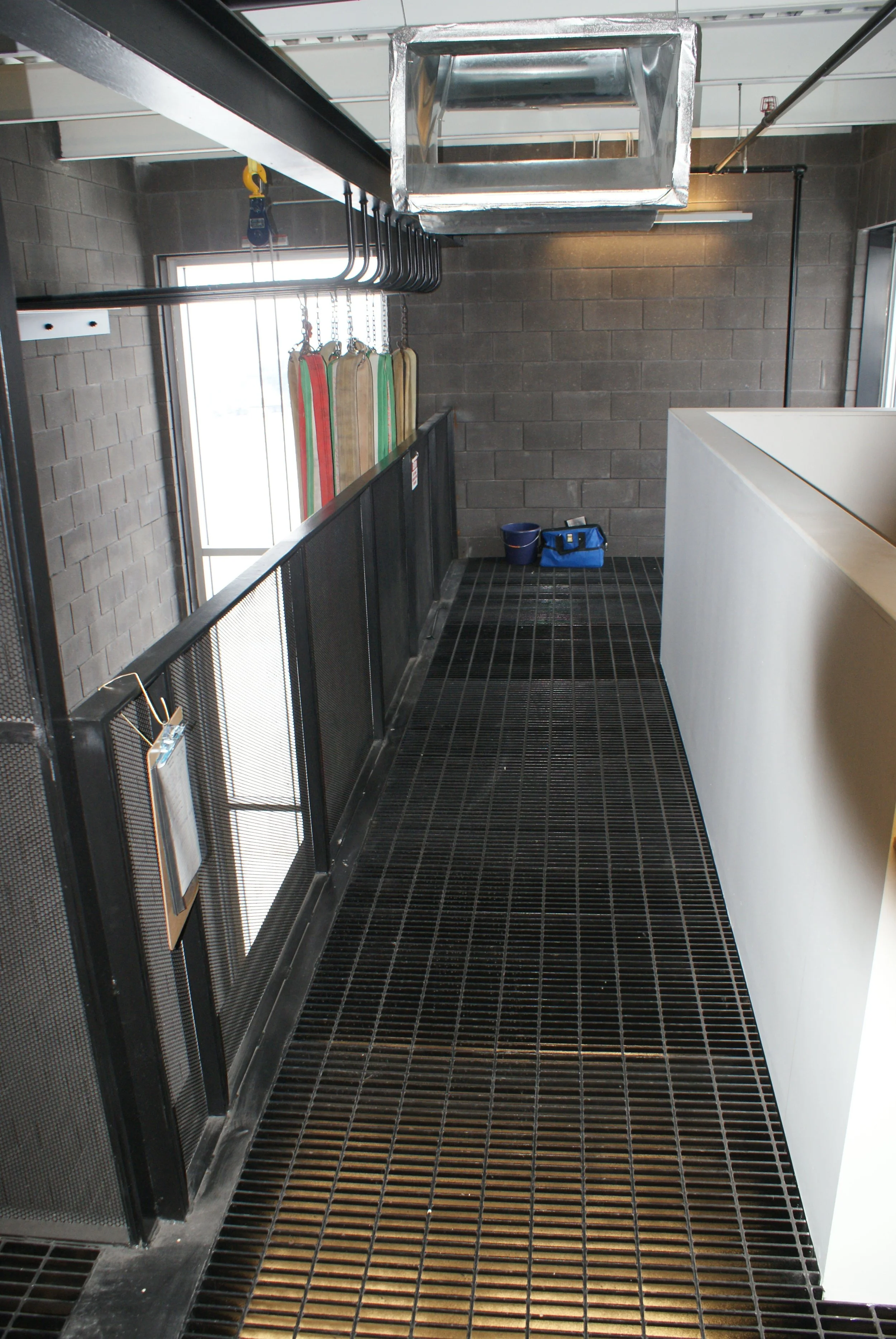 Industrial laundry room with a grated black floor, a black metal railing, hanging cleaning accessories, and a window