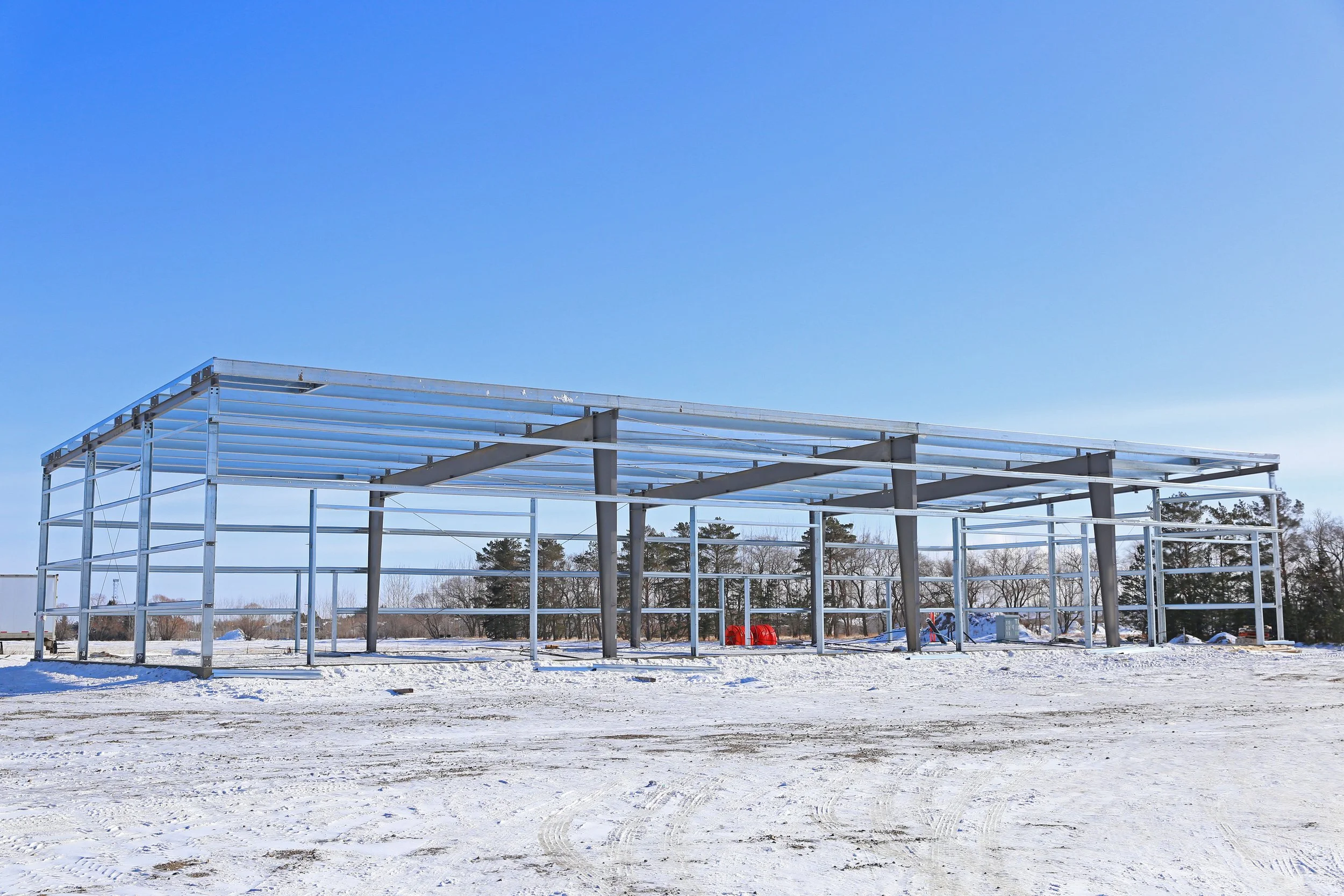 Steel framework of a building under construction in snowy landscape during clear blue sky.