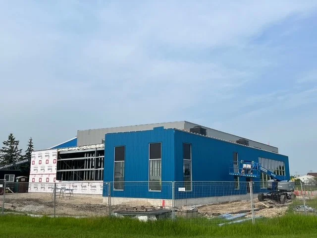 Construction site of a modern blue commercial building under development, with a large lift and construction materials around.