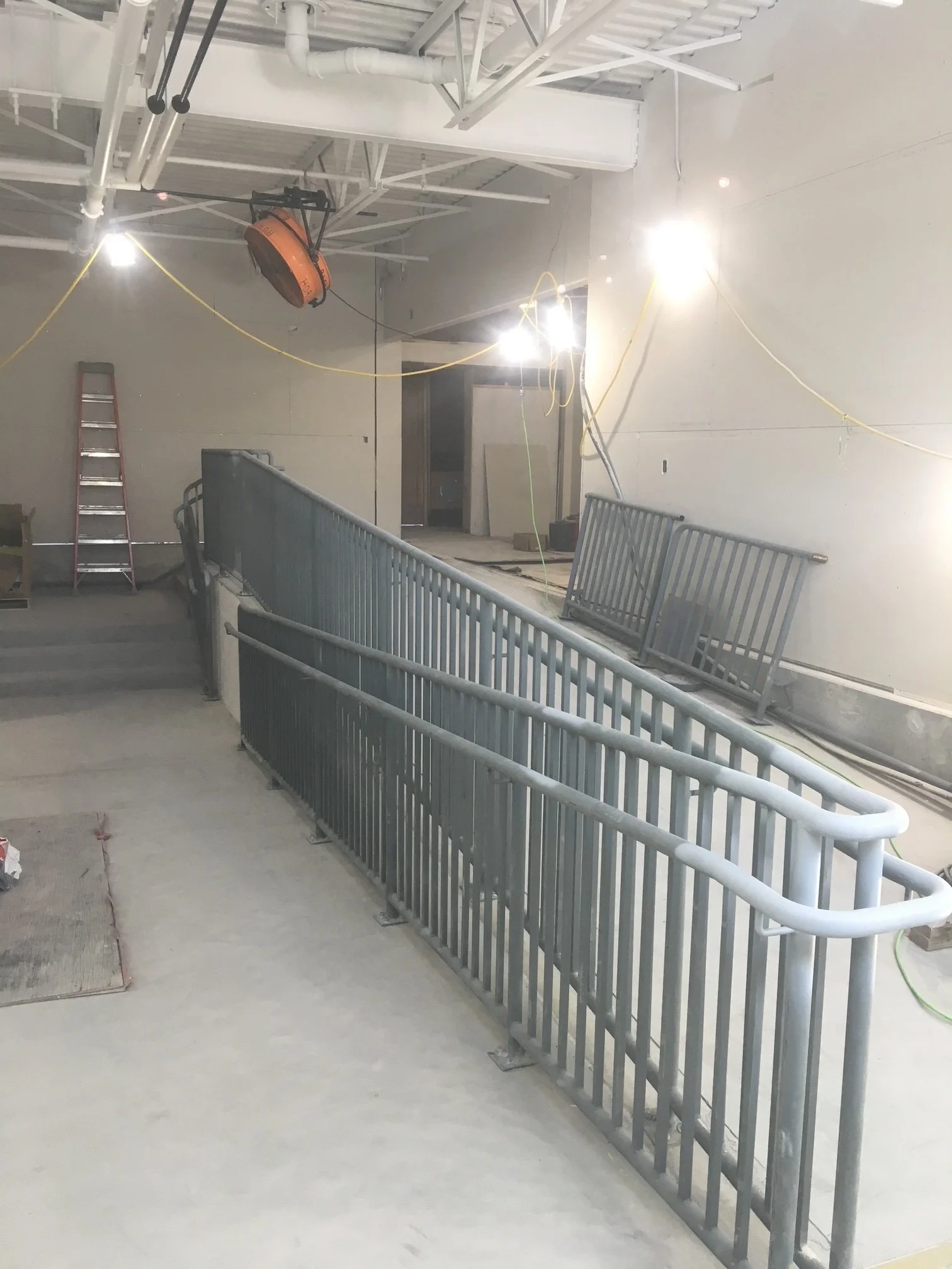 Construction site with metal railing, ladder, construction lights, and unfinished walls.