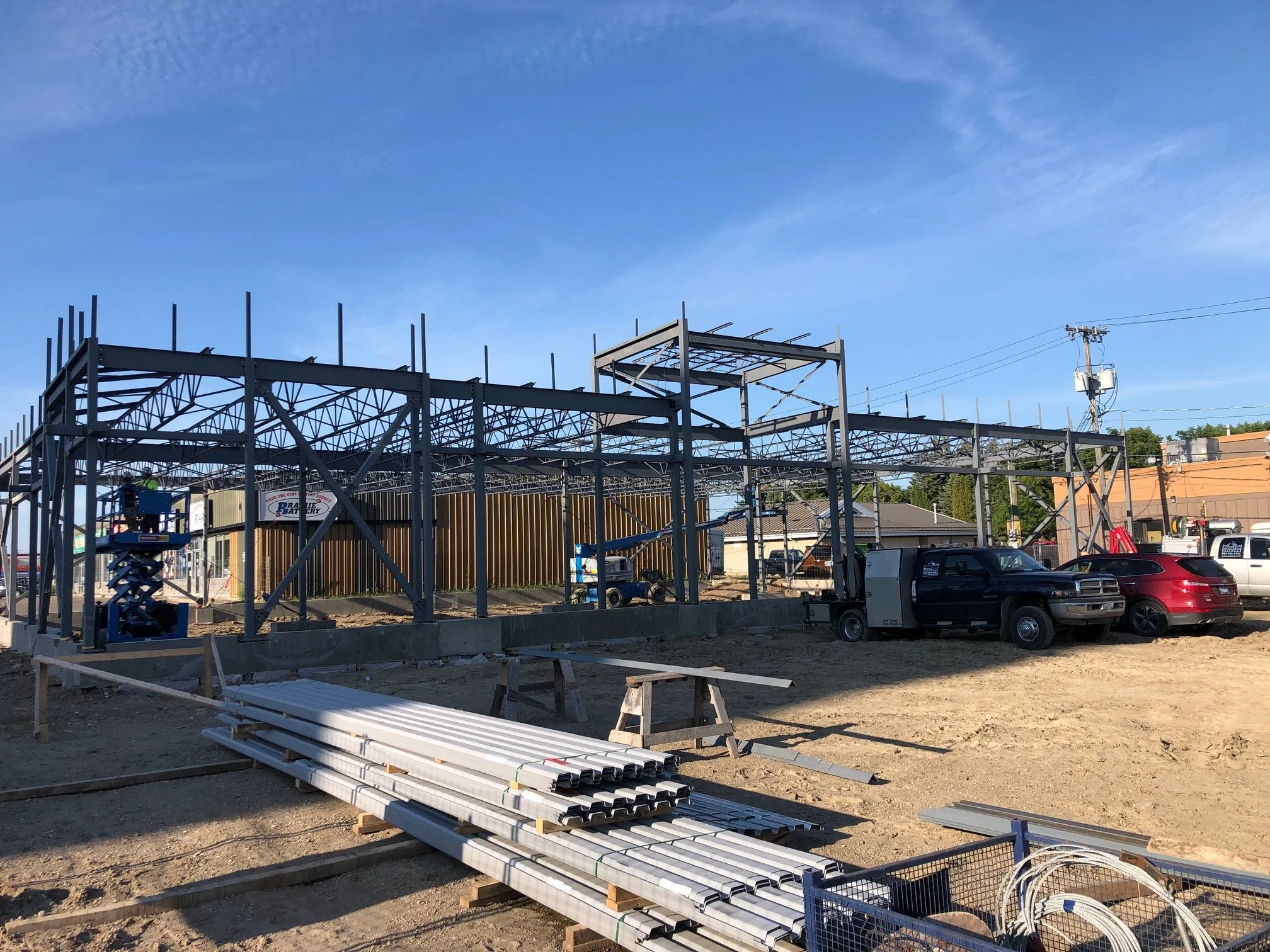 Construction site with steel framework, trucks, and construction materials under a clear blue sky.
