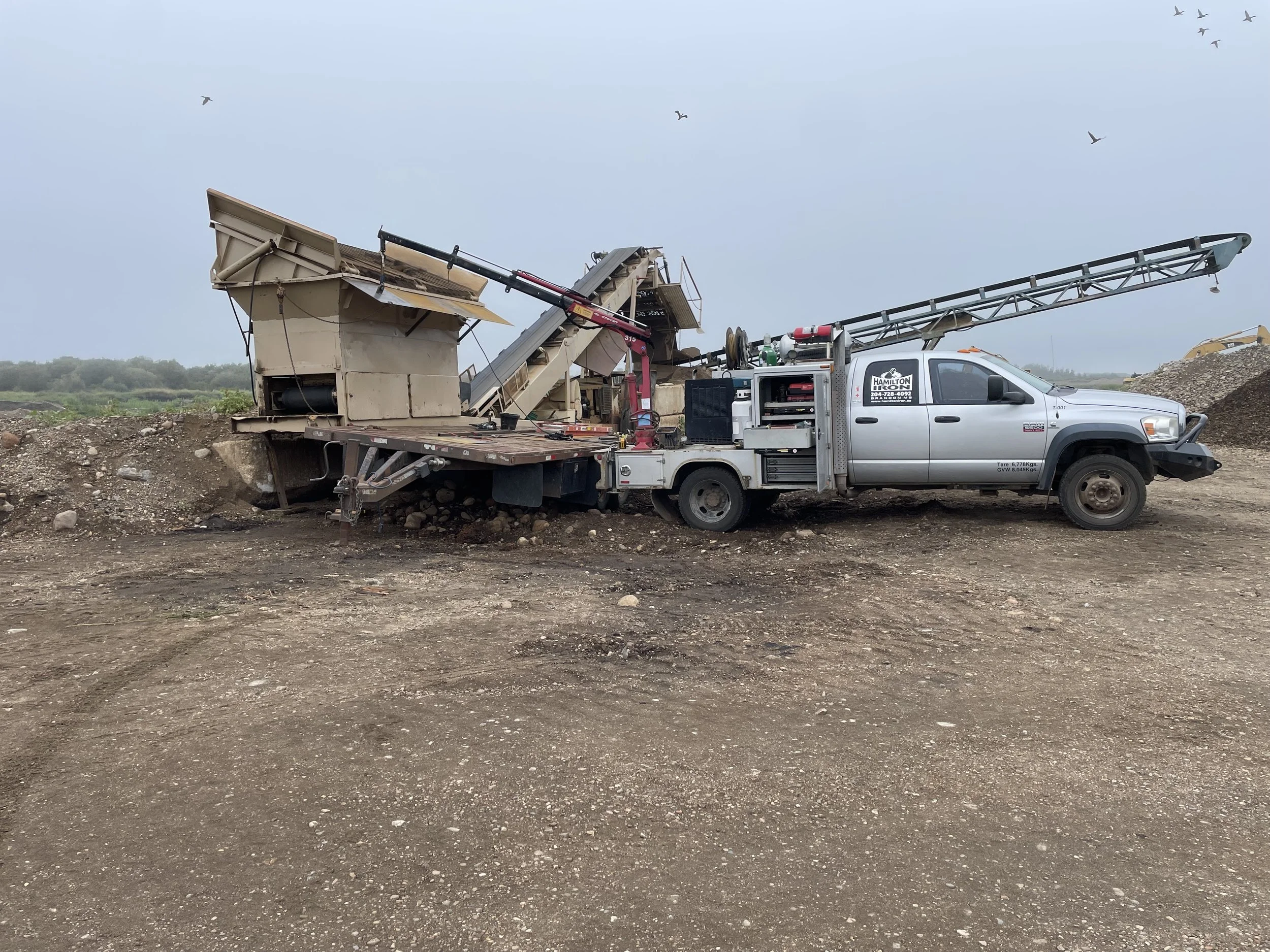 A bucket-wheel excavator connected to a service truck on a construction site with dirt and rocks.