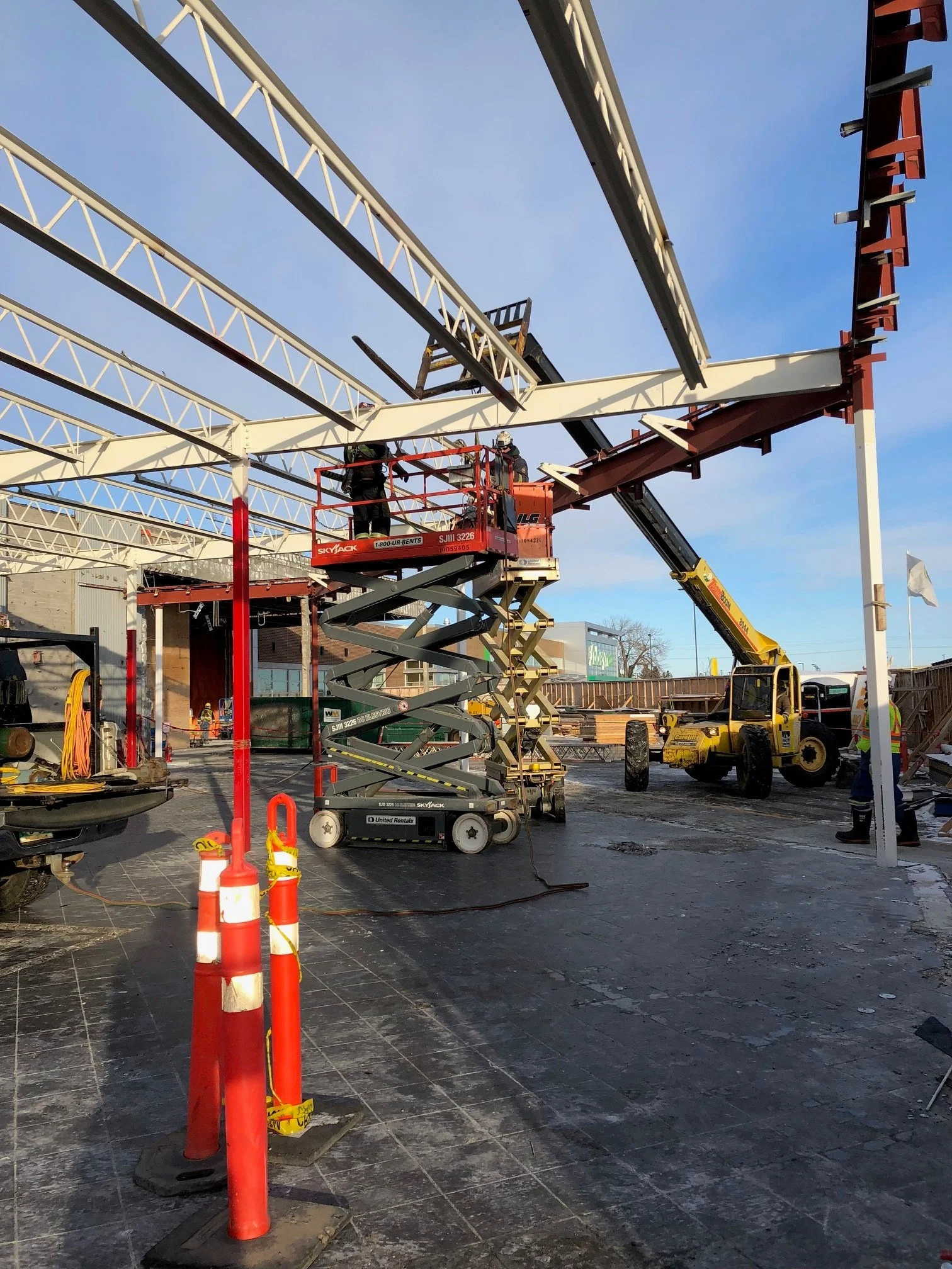 Construction workers using a scissor lift and crane to assemble a metal framework structure outside on a clear day