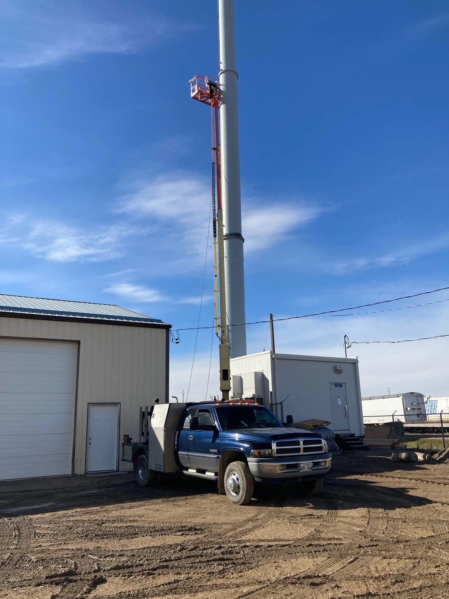 A work truck with a crane is parked next to a large cell tower being installed or serviced, with a clear blue sky in the background.