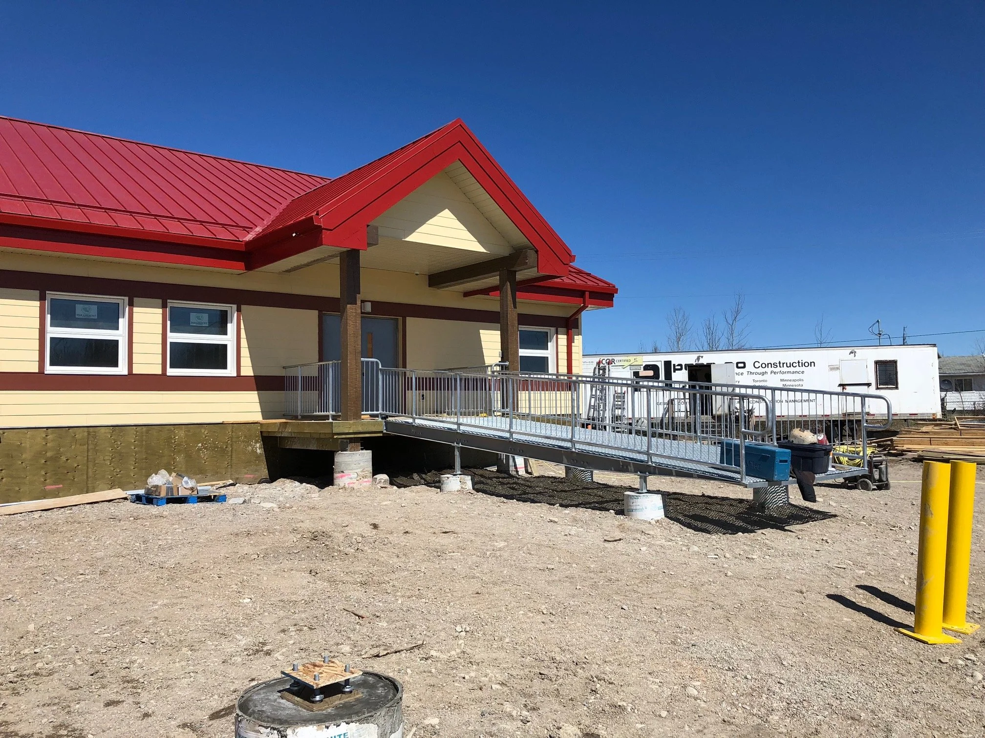 Construction site of a house with a newly installed wheelchair ramp, surrounded by construction equipment and materials.