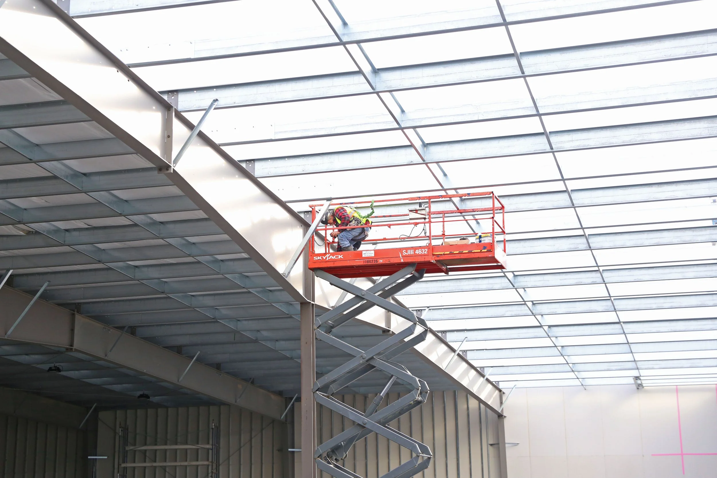 Construction worker using a scissor lift to work on the ceiling of a large building under construction