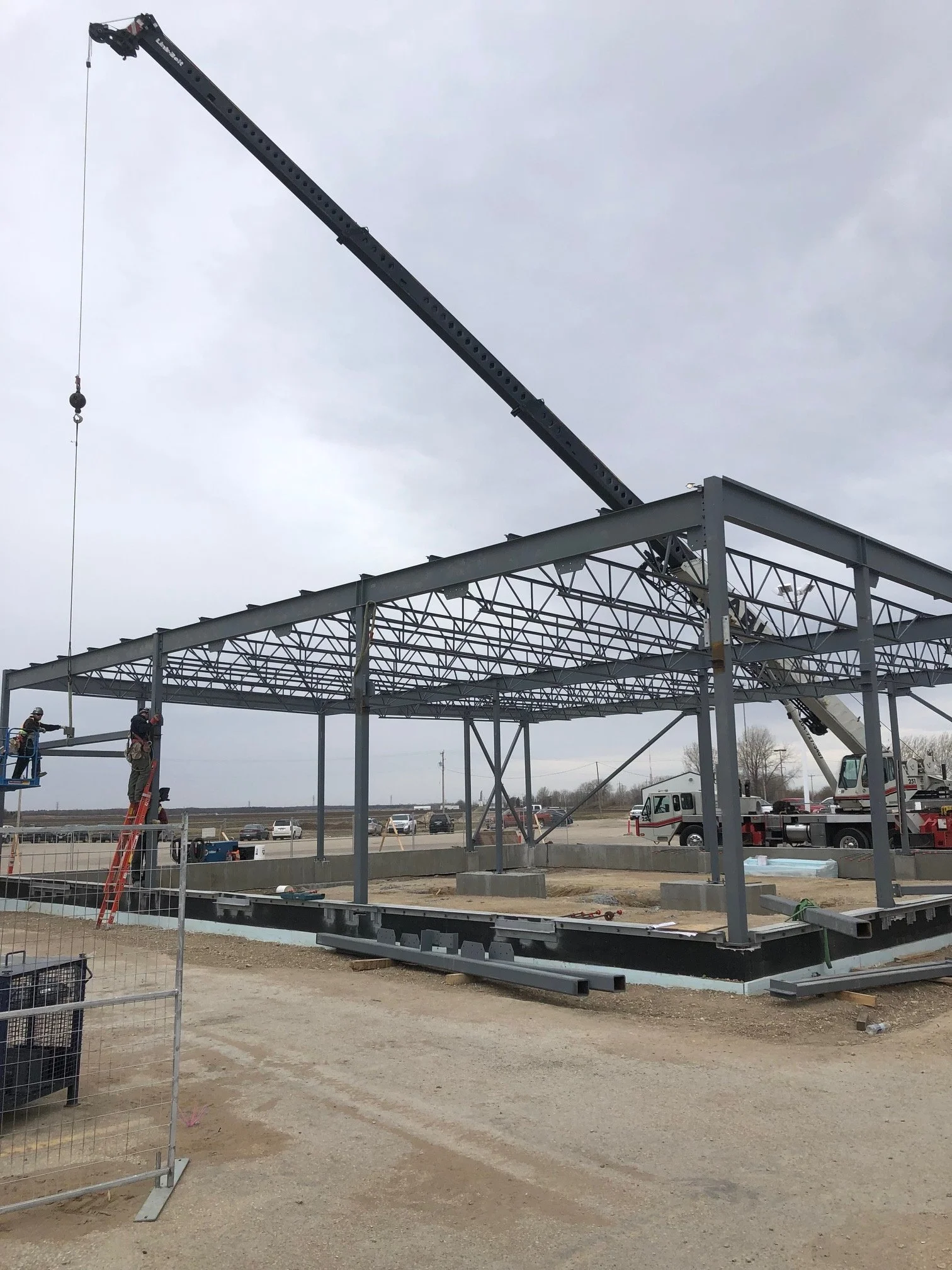 Construction site with steel framework and a crane lifting materials, overcast sky.