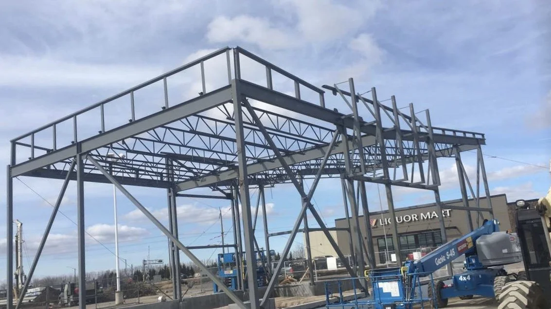 Steel framework of a building under construction at a commercial site with a liquor market in the background.