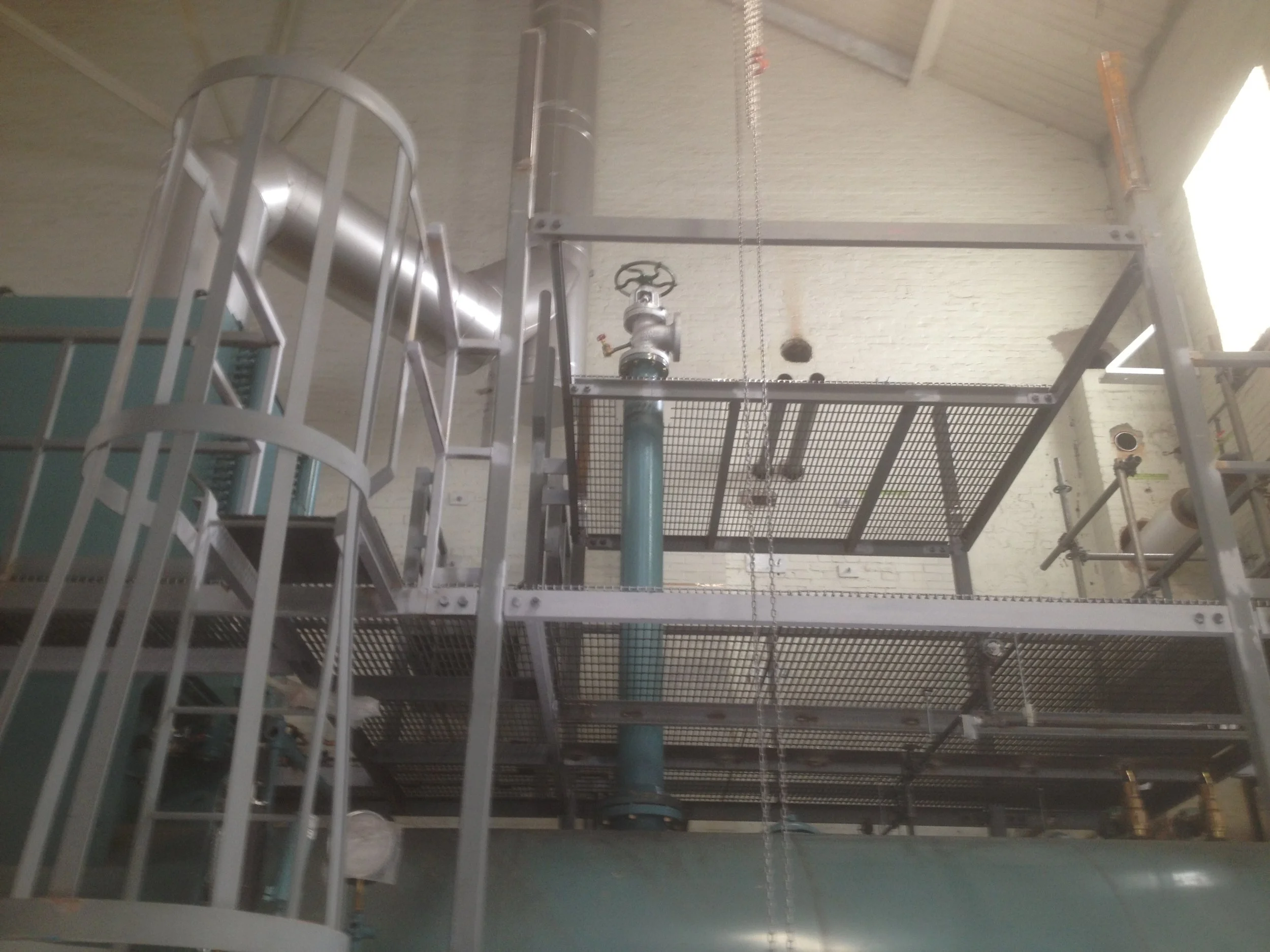 Industrial piping system with a large blue pipe, a metal valve, and metal support structures in a factory or plant setting.