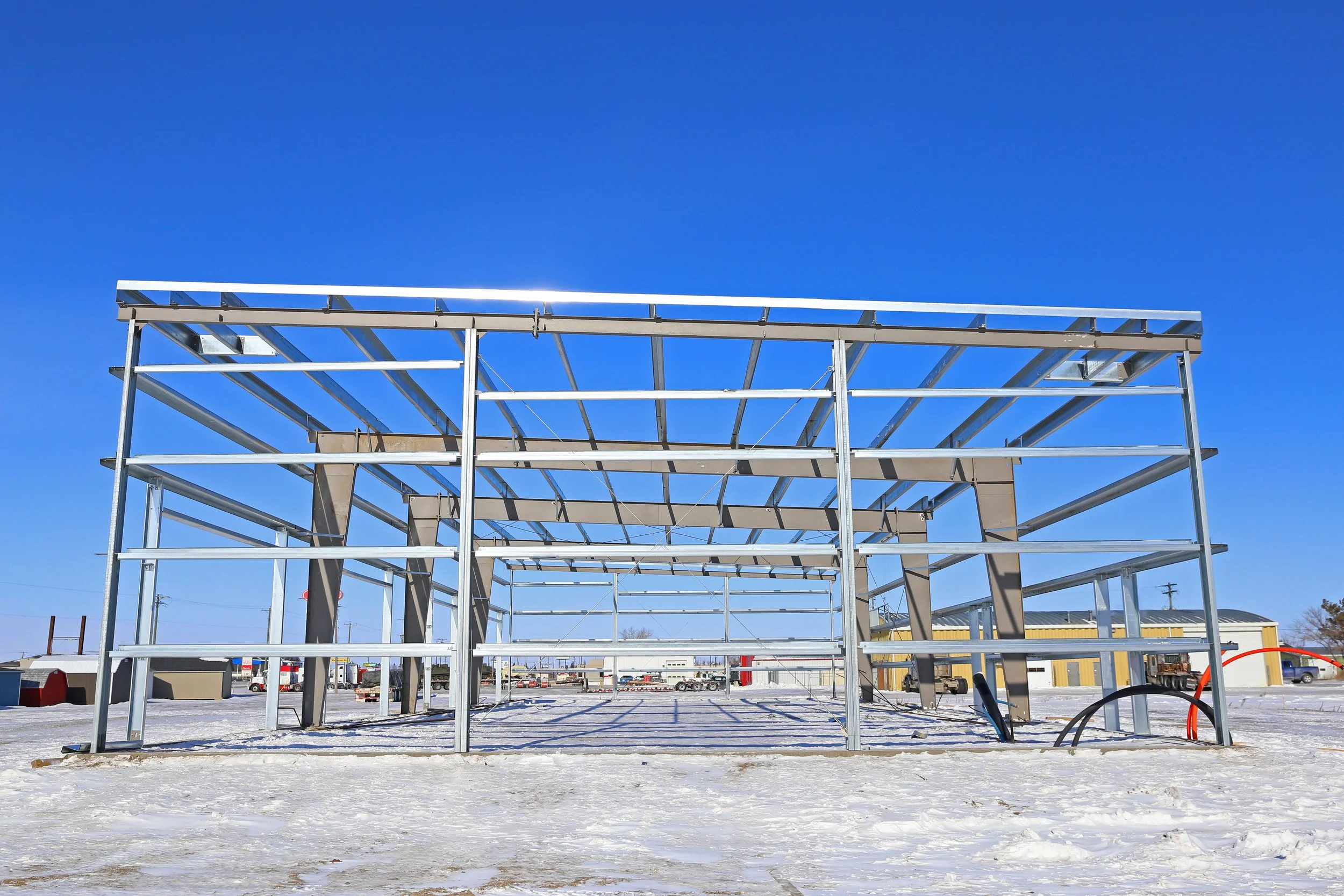 Steel framework of a building under construction on a snow-covered ground with a clear blue sky in the background.