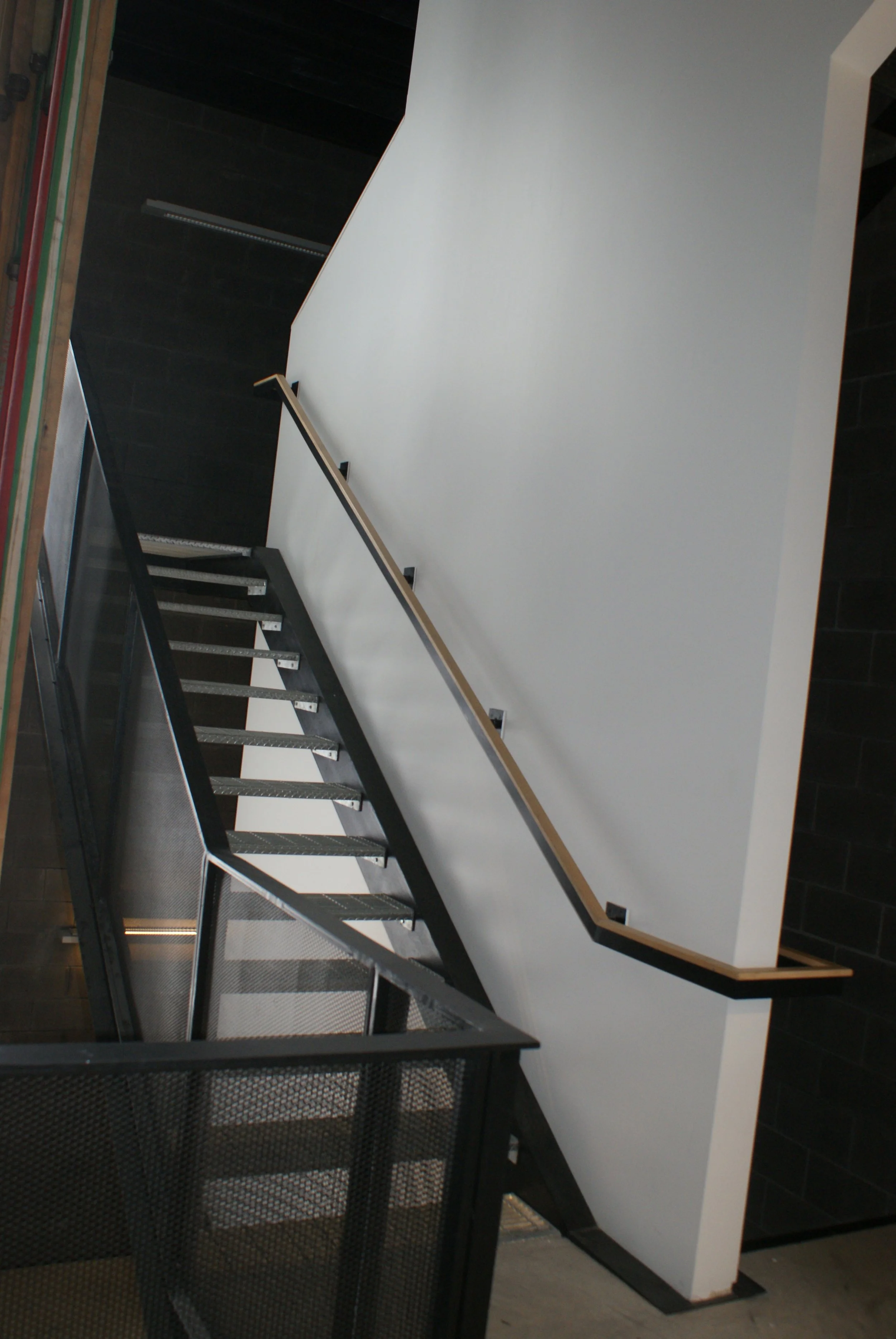 Indoor staircase with black metal frame, open risers, and wooden handrail on a white wall.