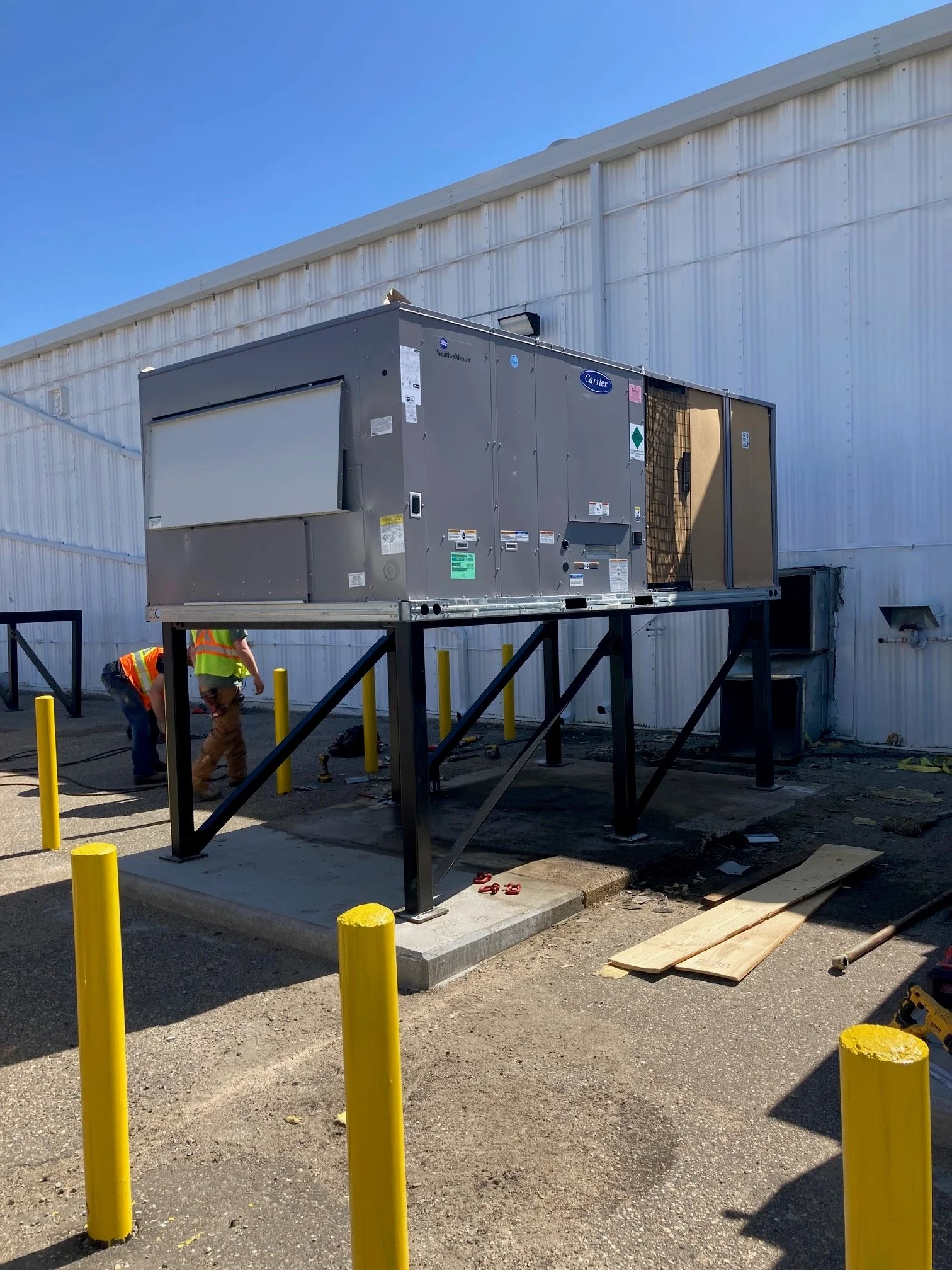 Industrial HVAC unit on a raised platform outside a metal building with workers nearby.