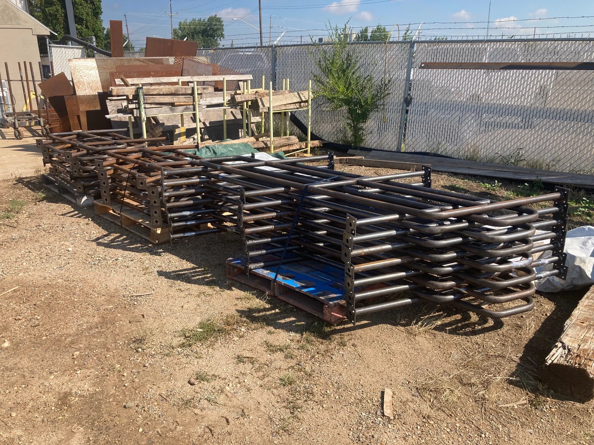Stacks of metal pipes and scaffolding frames on pallets in an outdoor yard.