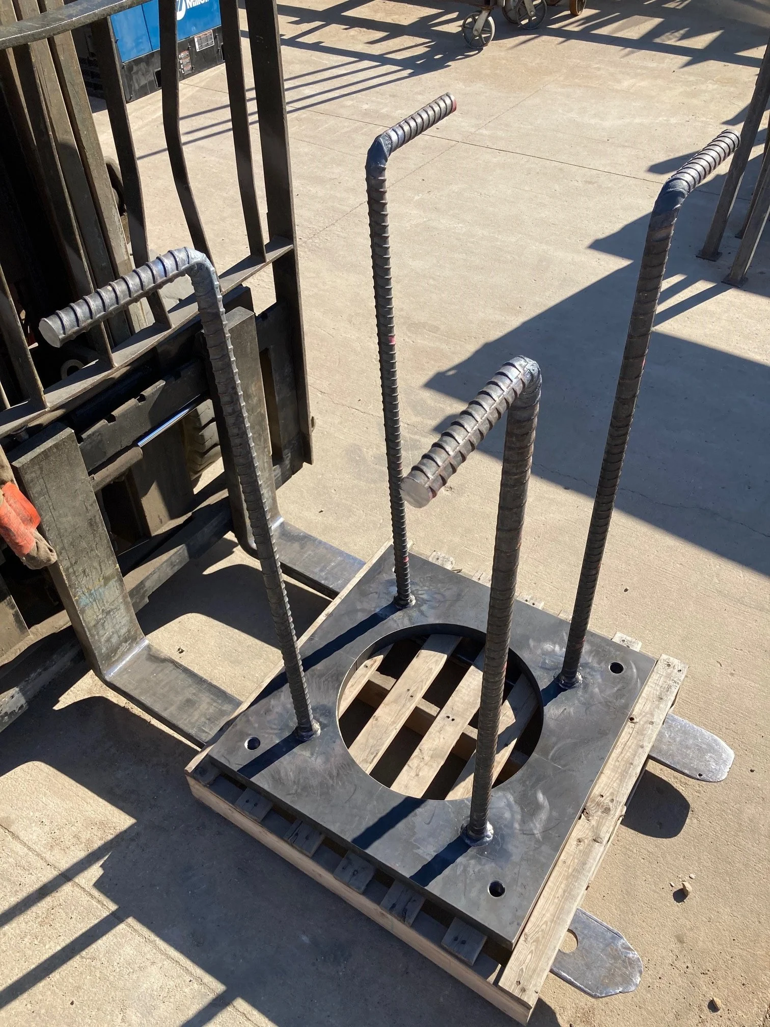 A metal square platform with four vertical rebar rods, used as a form for concrete, outdoors on a concrete surface.