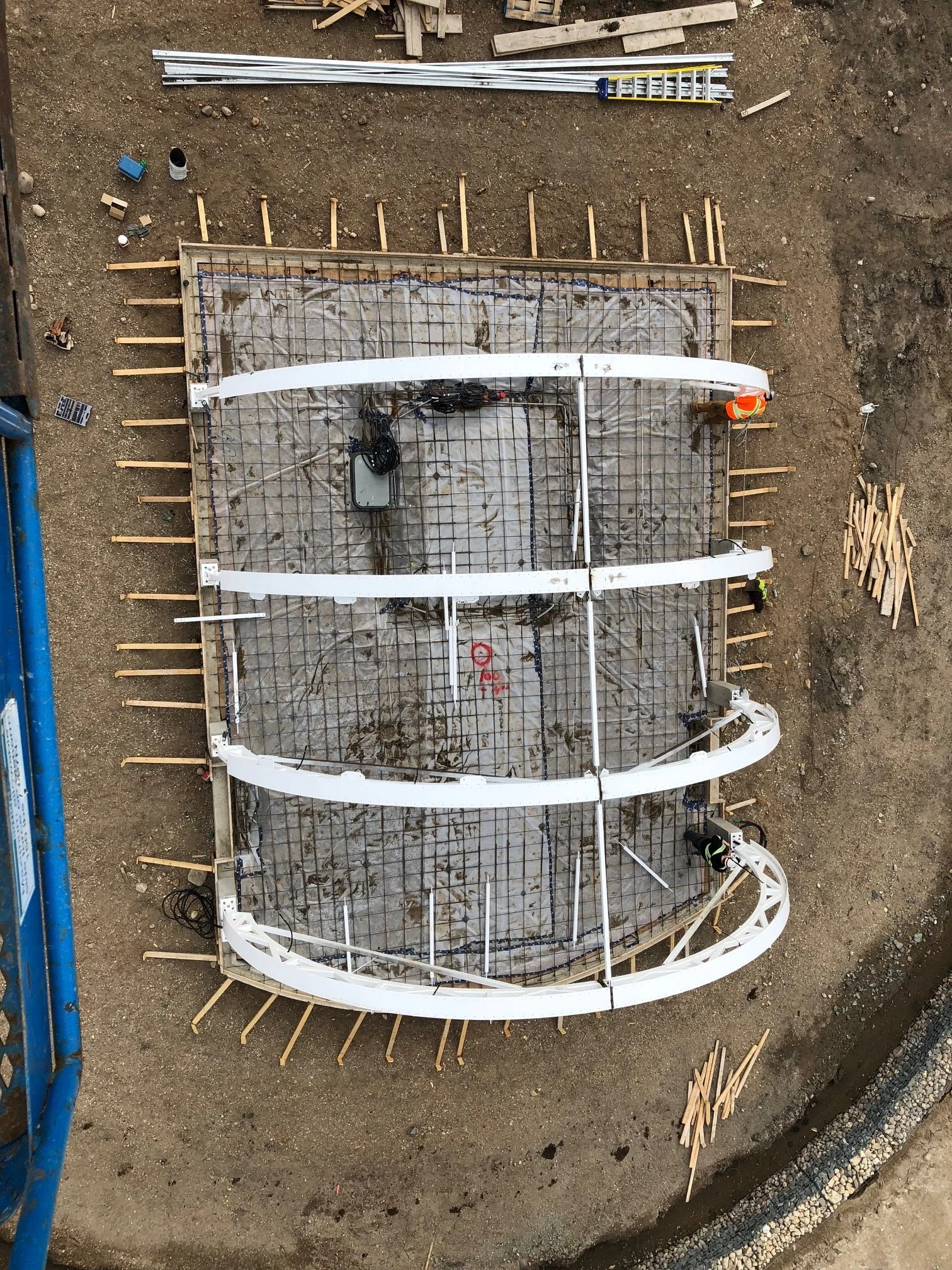 A construction site from above showing a curved framework, with scaffolding and metal reinforcements, and workers in safety vests nearby.