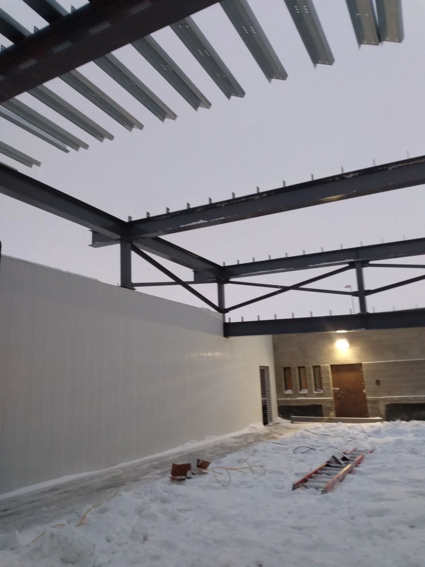 Construction site with steel framework and snow-covered ground at dusk.