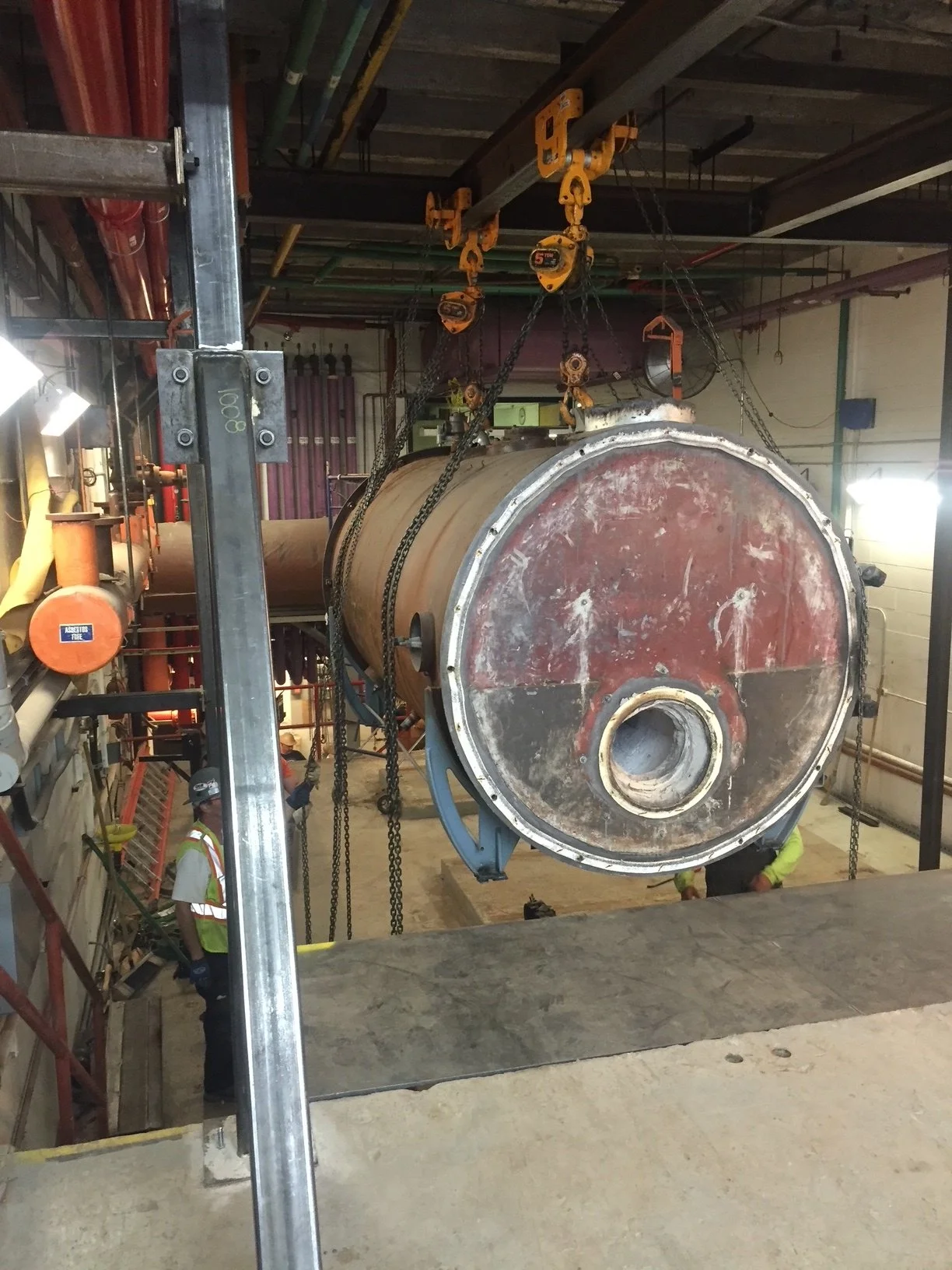 Large industrial tank or pressure vessel being lifted and installed inside a factory or industrial facility with workers nearby.