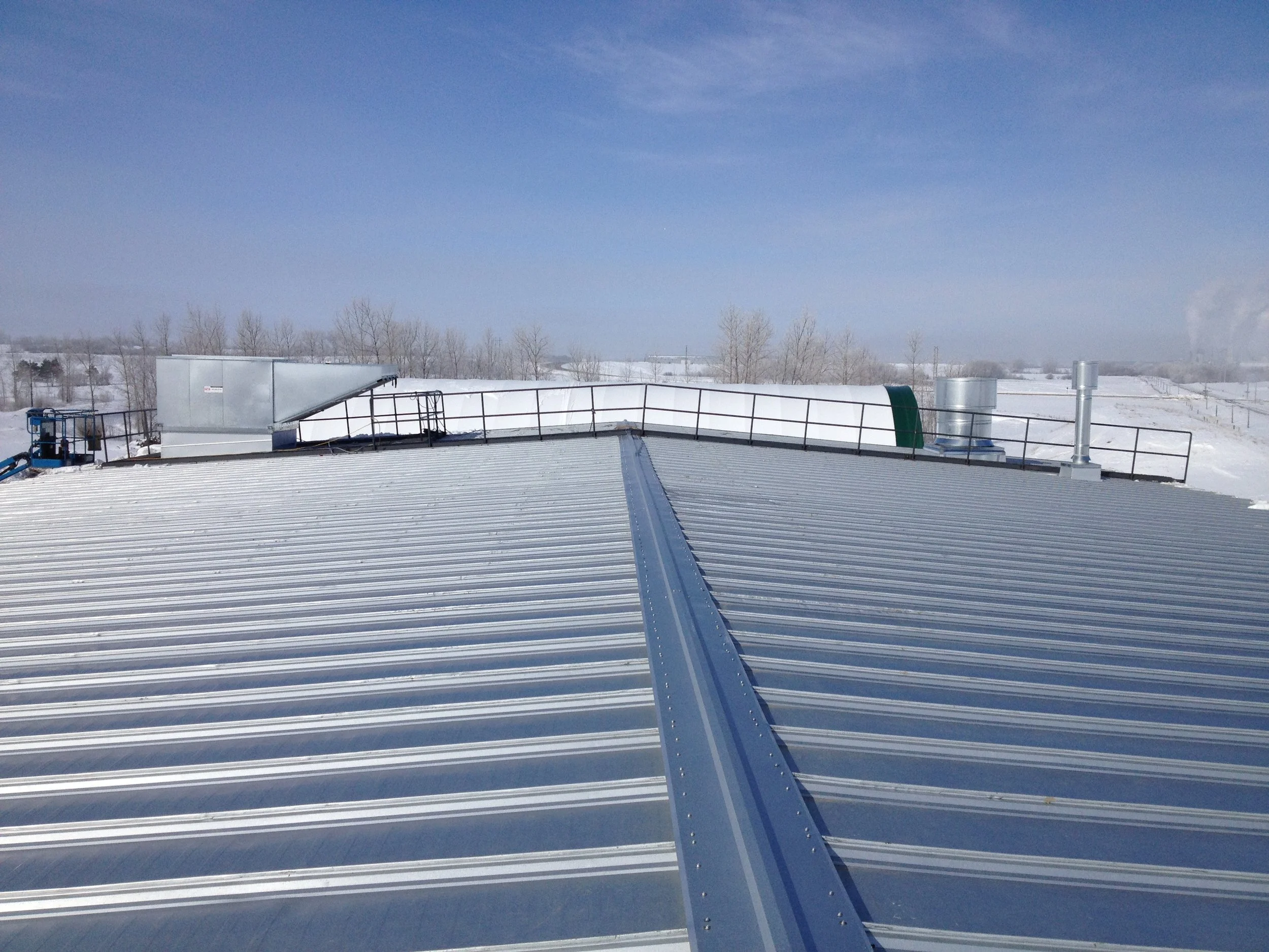 Metal rooftop with snowy landscape and clear blue sky in the background.