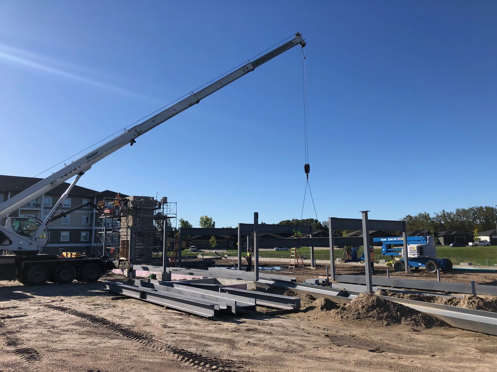 Construction site with a crane lifting steel beams and workers assembling a building frame on a clear, sunny day.