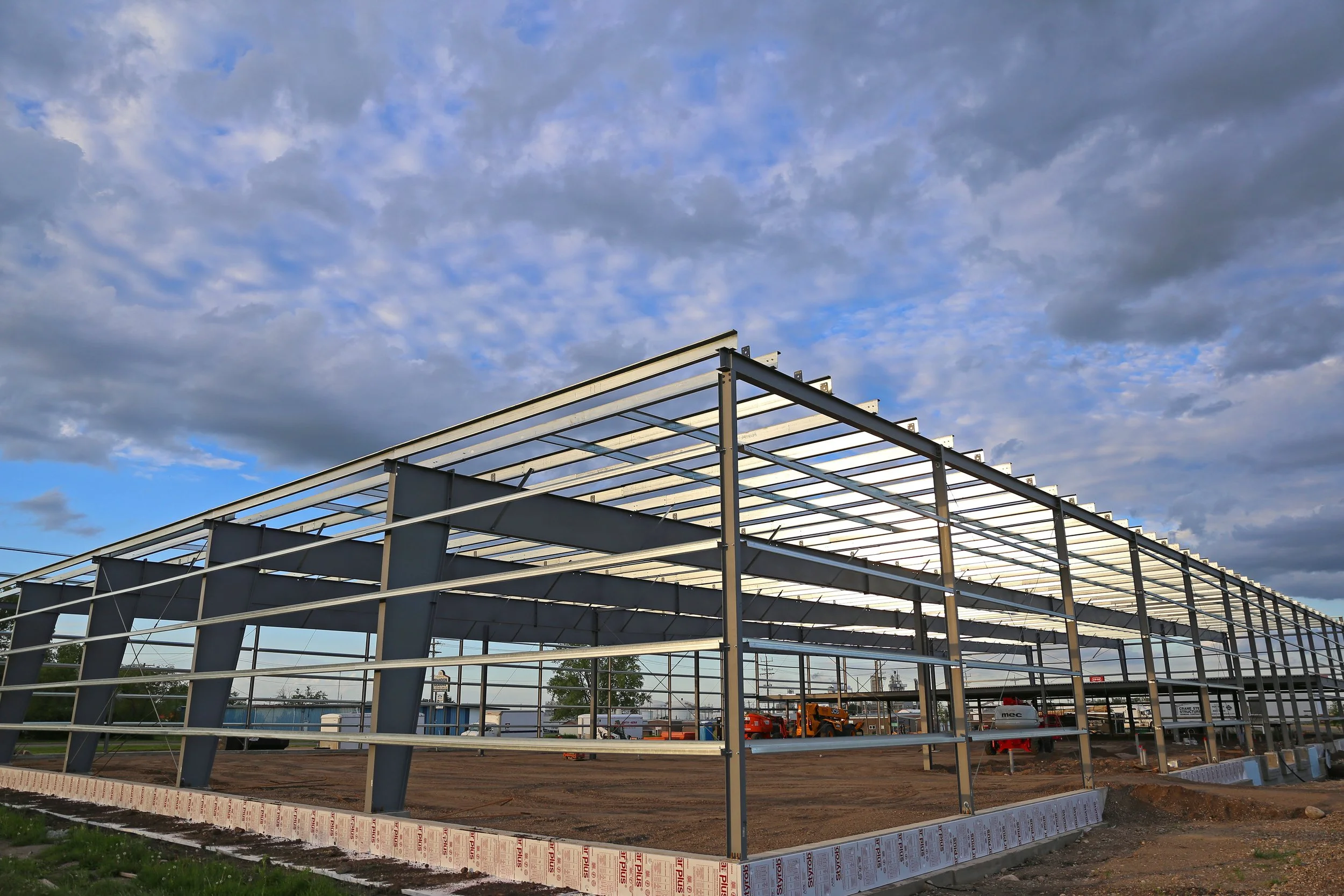 Steel framework of a building under construction with a cloudy sky above.