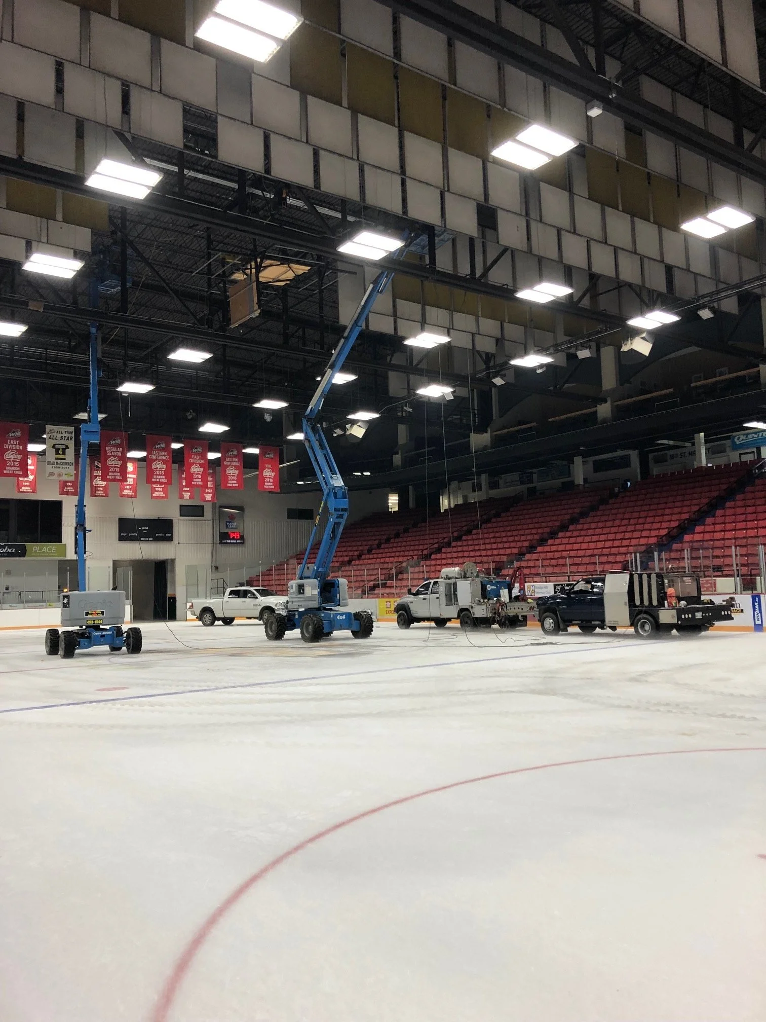 Ice hockey rink with maintenance equipment and vehicles, including lifts and trucks, on the ice surface.