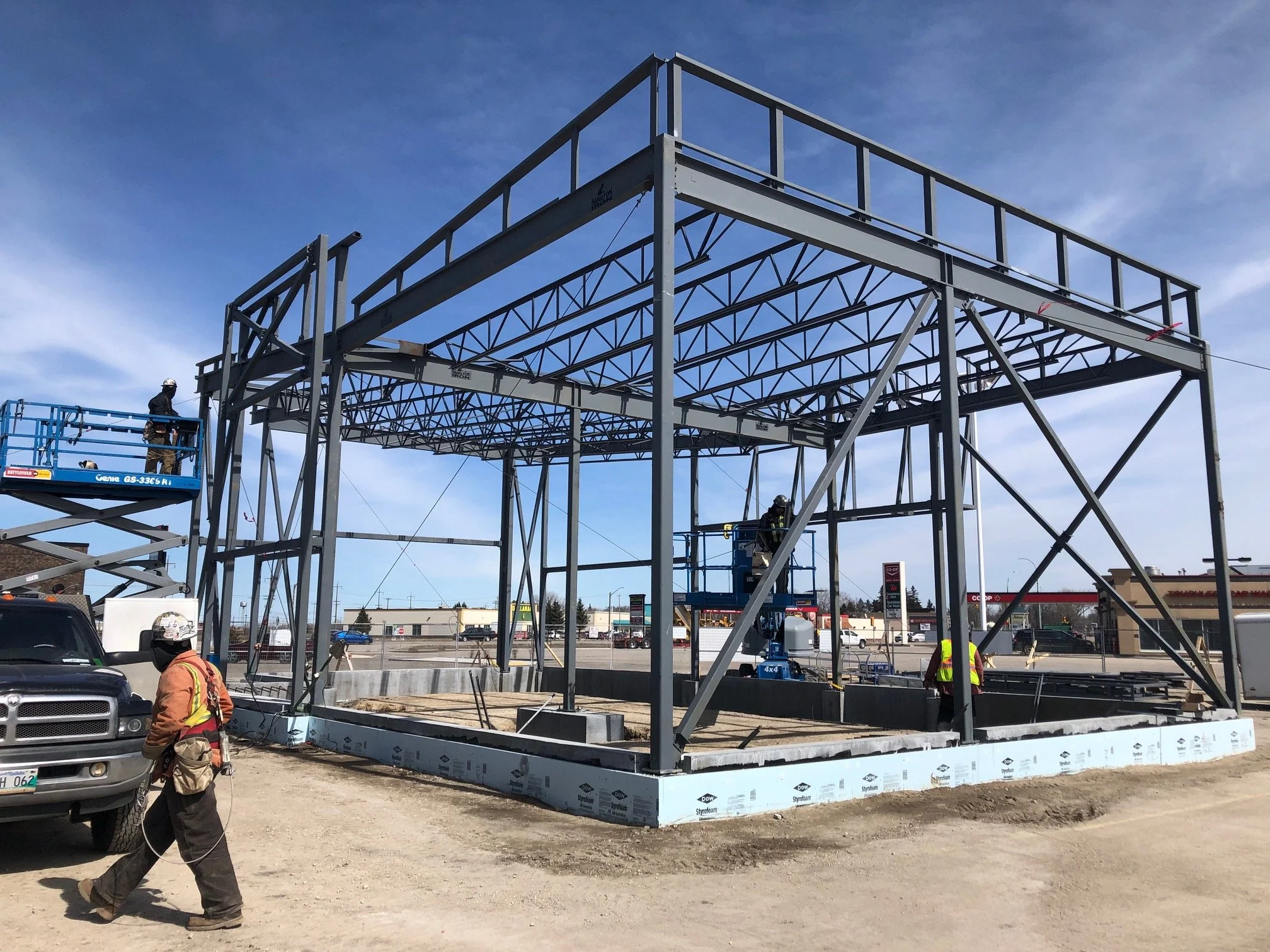 Steel framework of a building under construction with construction workers and machinery present.