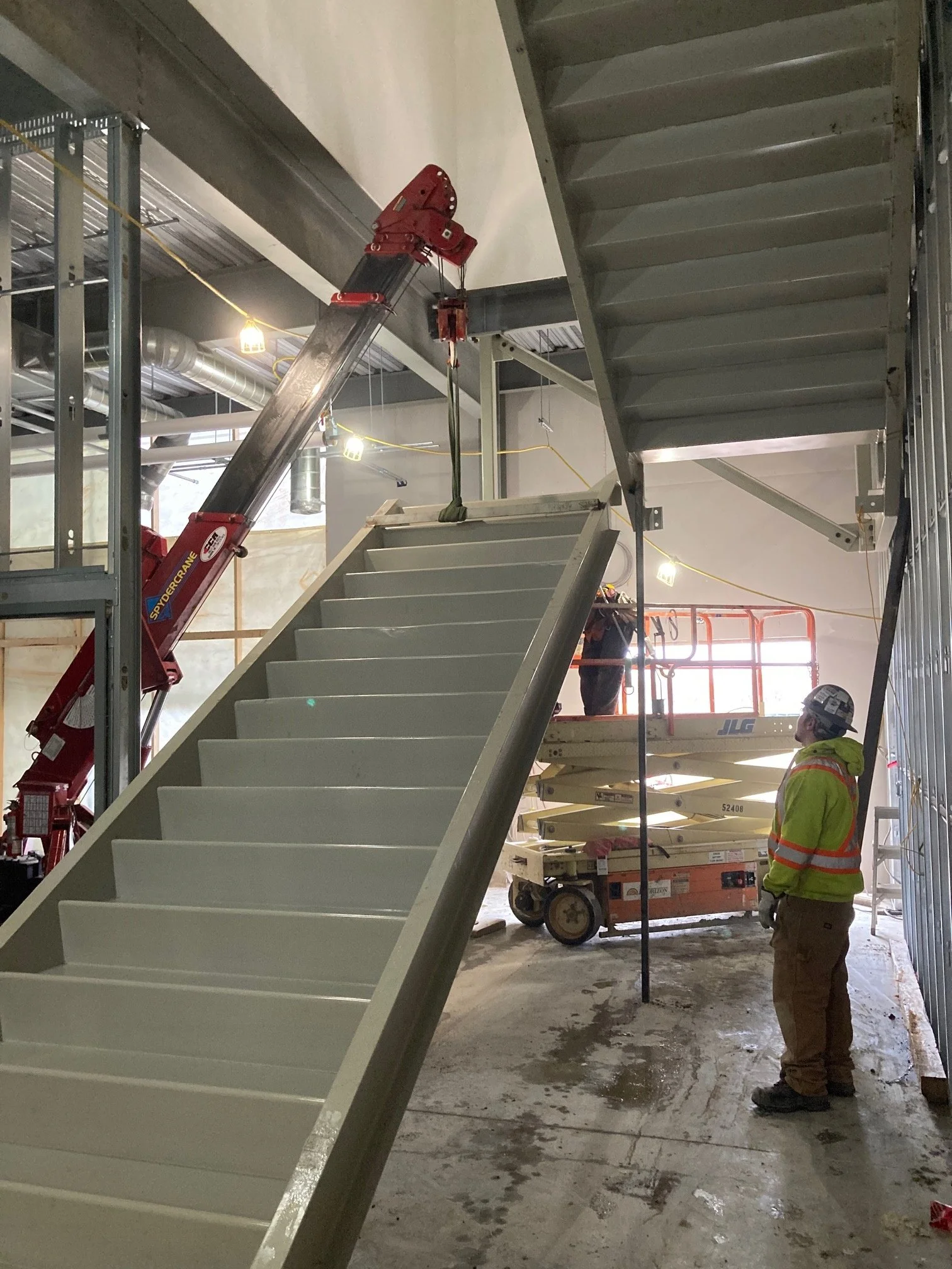 Construction workers installing a staircase with a crane in an indoor construction site.
