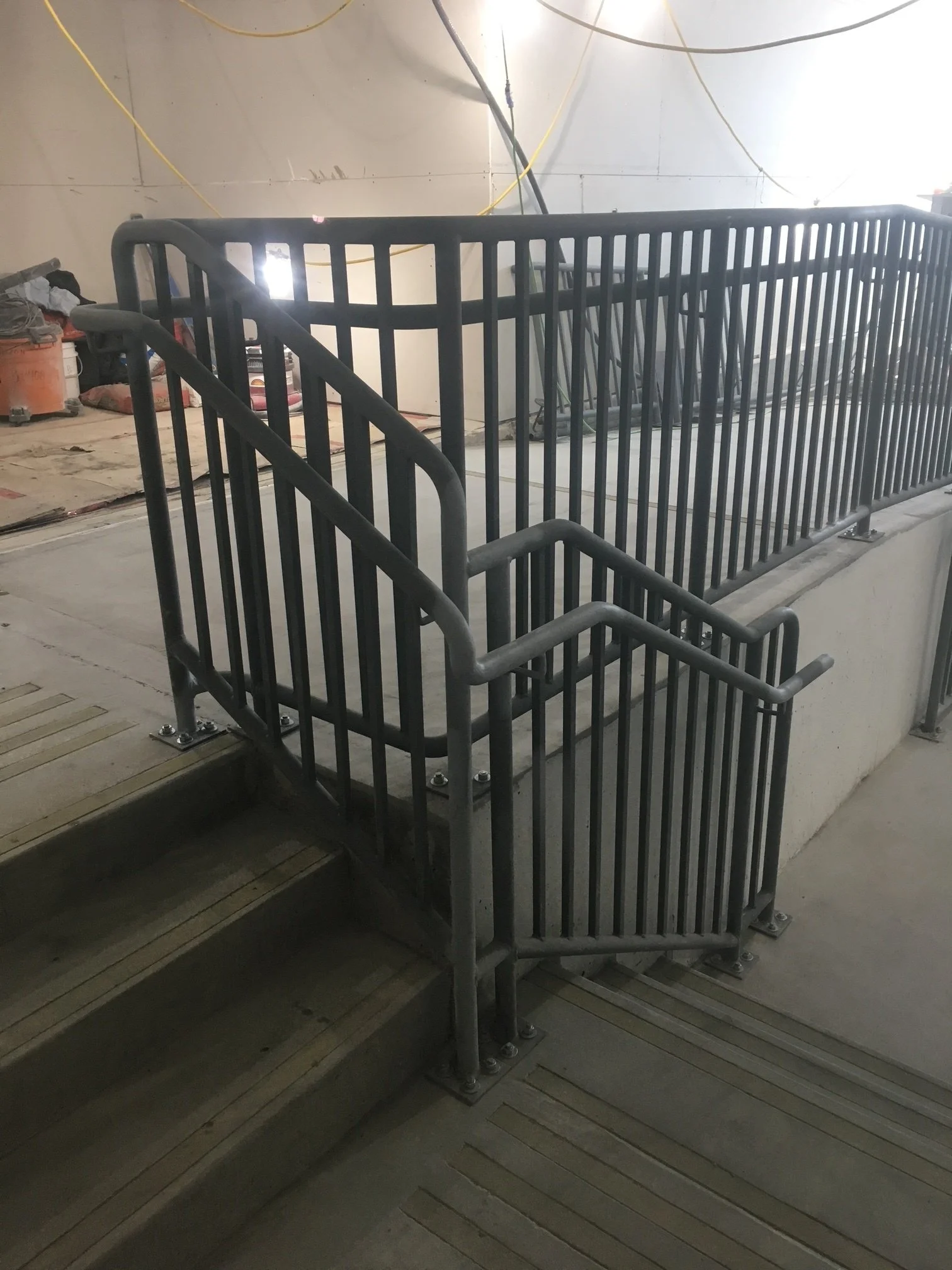 Metal safety railing installed at the top of a staircase in an indoor construction area.