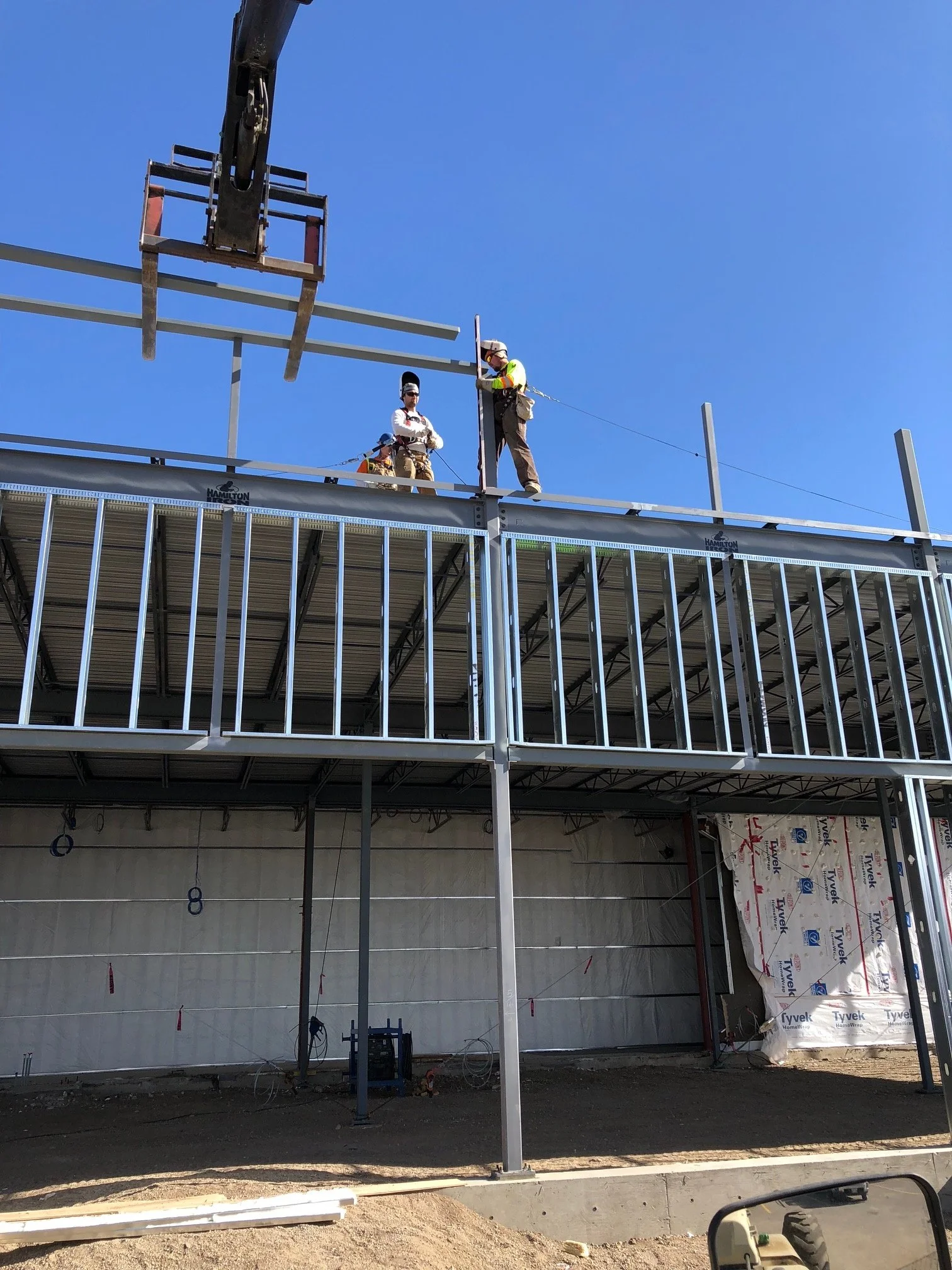 Construction workers on the second floor of a building under construction, installing metal framing with a clear blue sky in the background.