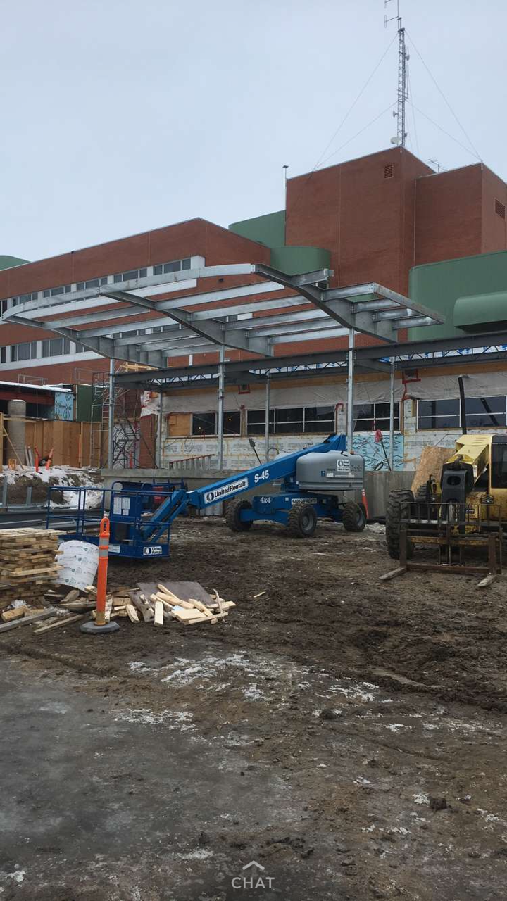 Construction site with machinery and building framework in progress outside a large brick building.