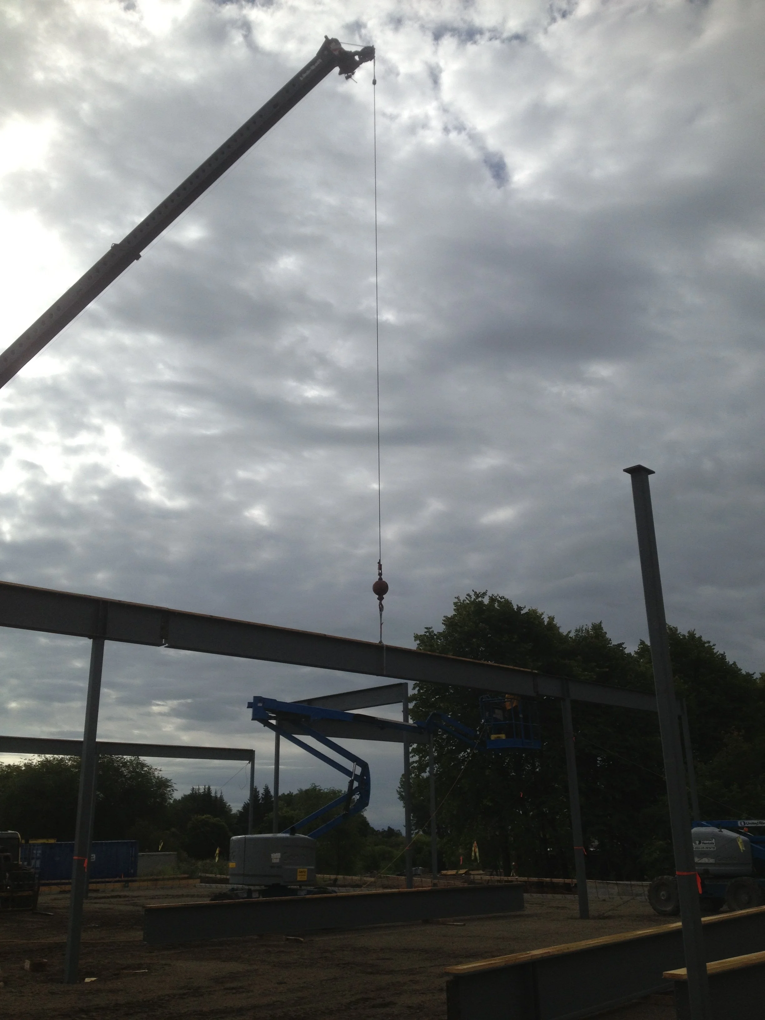 Construction site with steel beams, a crane, and a scissor lift under cloudy skies.