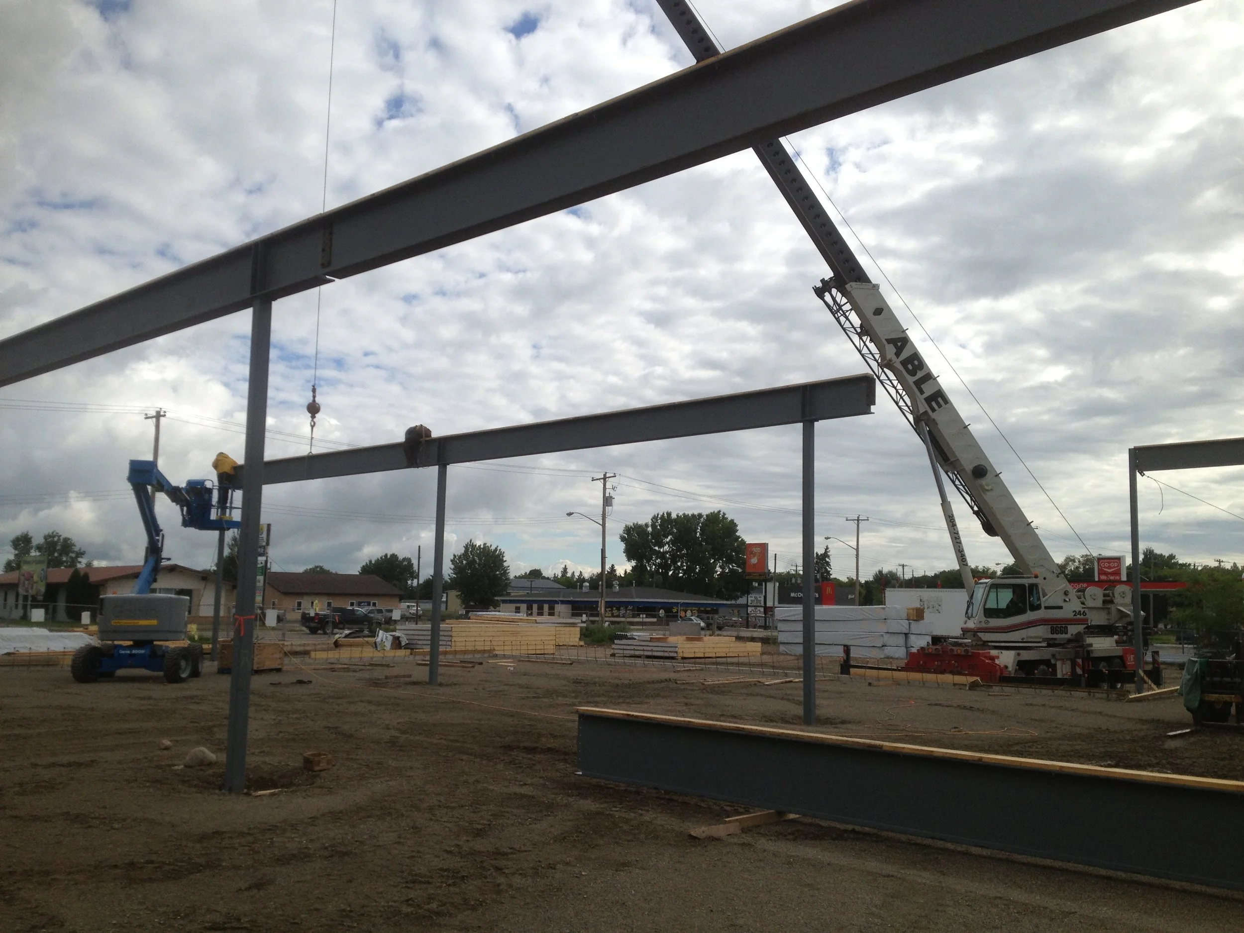 Construction site with steel beams being assembled, a crane, and workers working on a building framework under a cloudy sky.