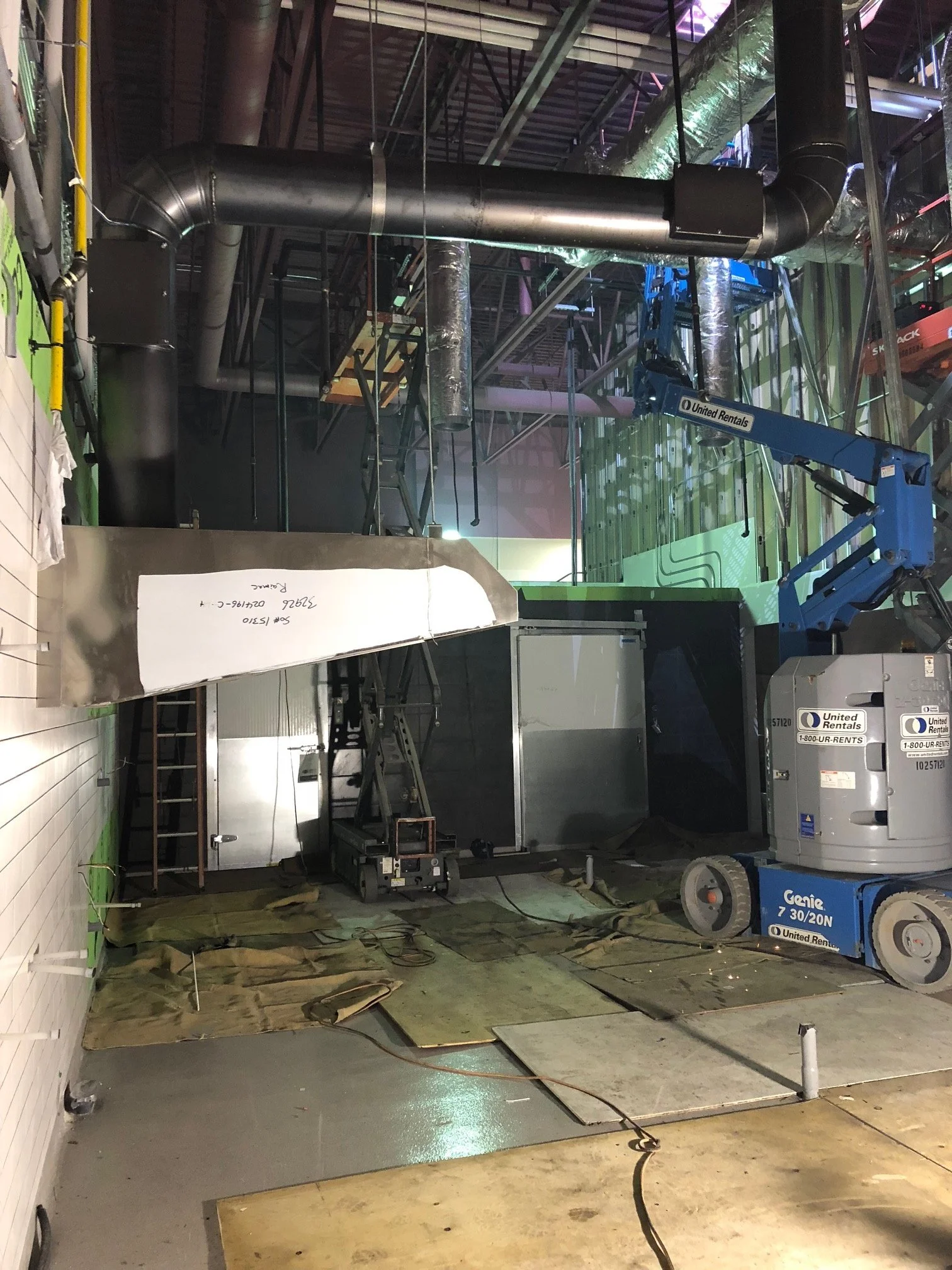 Construction site with exposed ductwork, a blue lift, and construction materials.