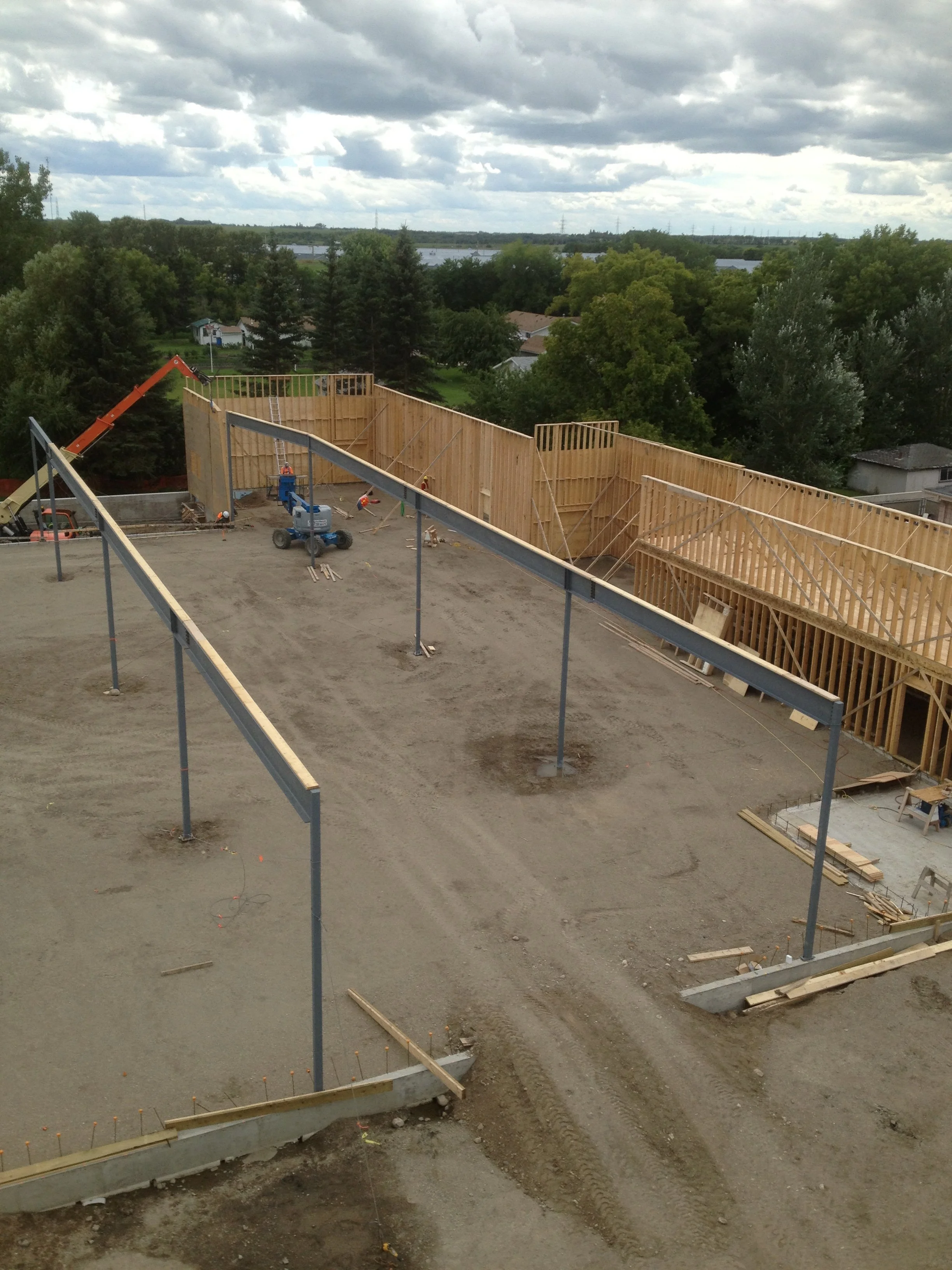 Construction site with wooden framing for a building, scaffolding, and construction equipment, with trees and water in the background.