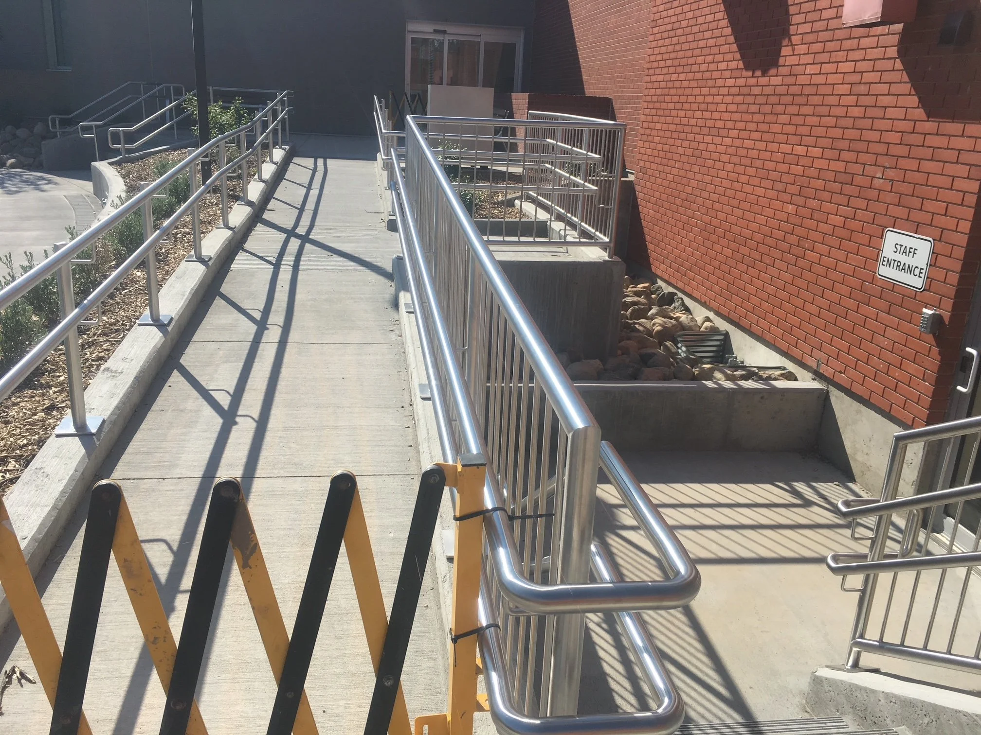 Wheelchair accessible ramp with metal railings leading to a building entrance marked 'Staff Entrance'.