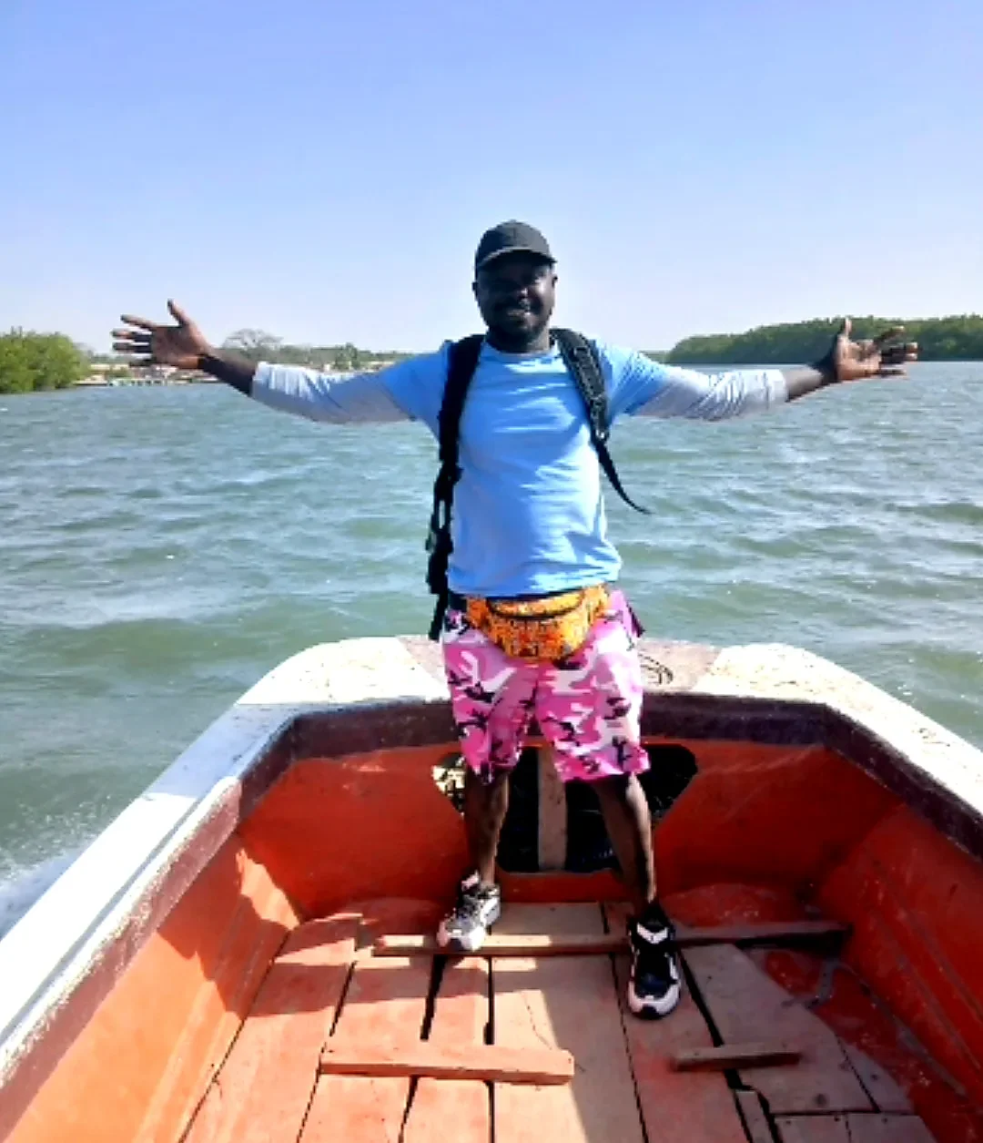 Saikou staat met open armen op een boot in Casamance, Senegal.