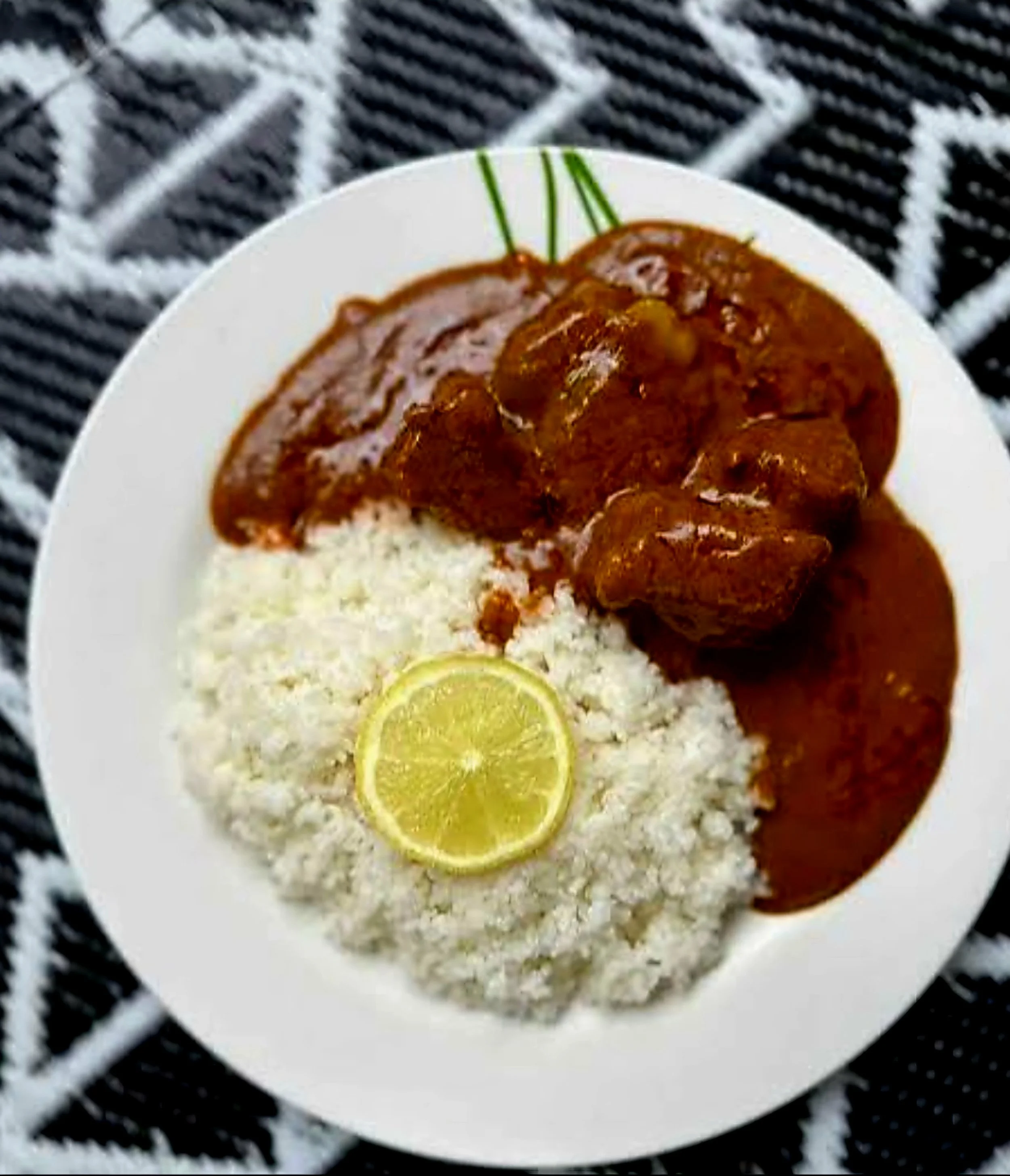 Domoda from Senegal served with white rice, a rich sauce, and a slice of lime on a white plate.