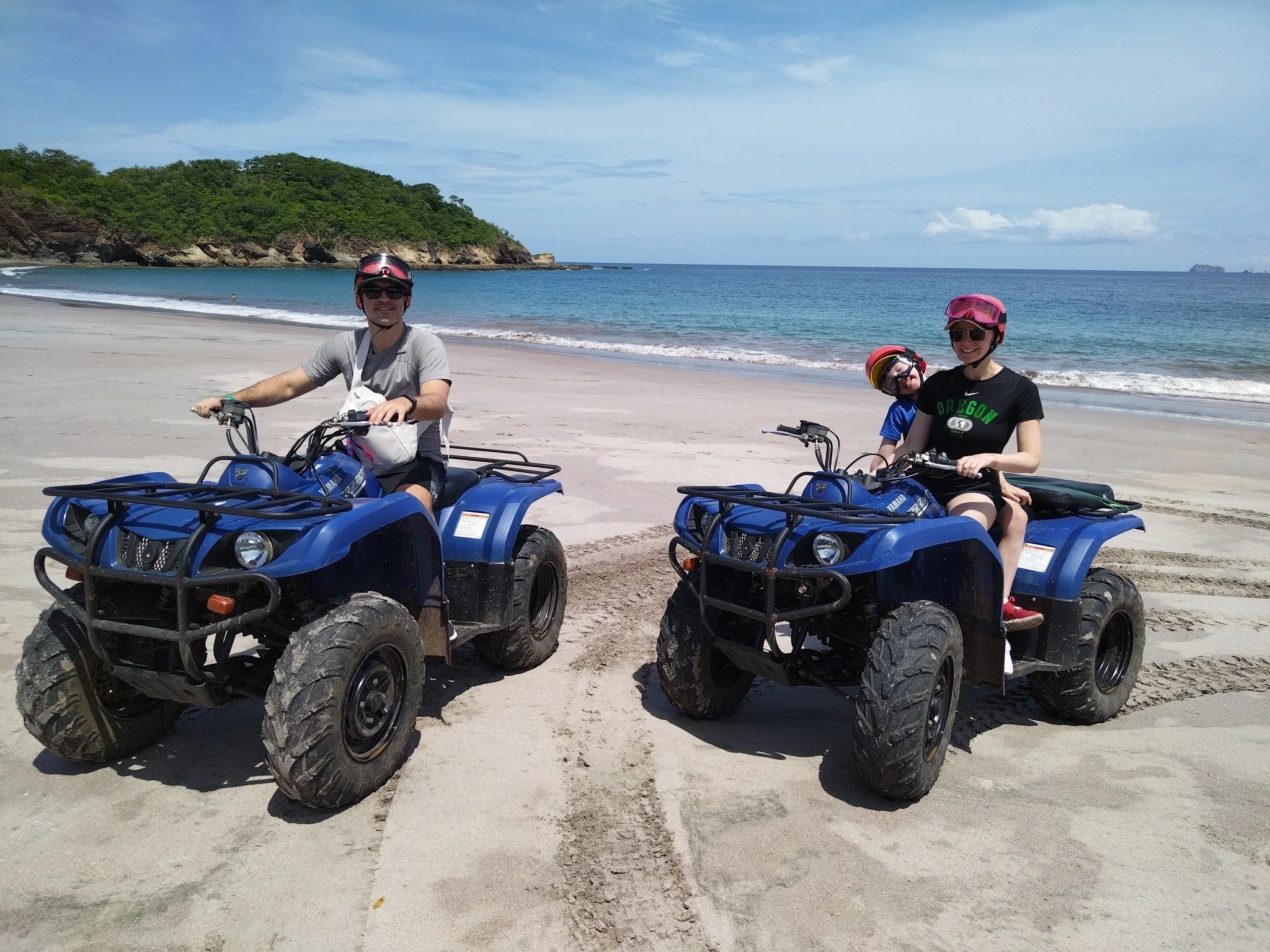 Dos adultos y un niño en cuatrimotos en la playa.