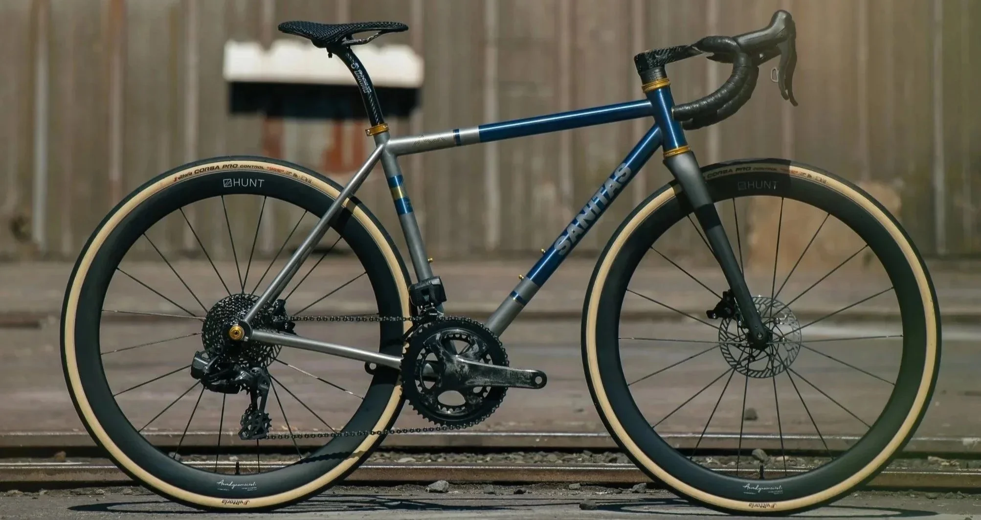 A blue and silver Santa Cruz mountain bike with black handlebars, cream-colored tires, disc brakes, and a black saddle, standing on a railroad track.