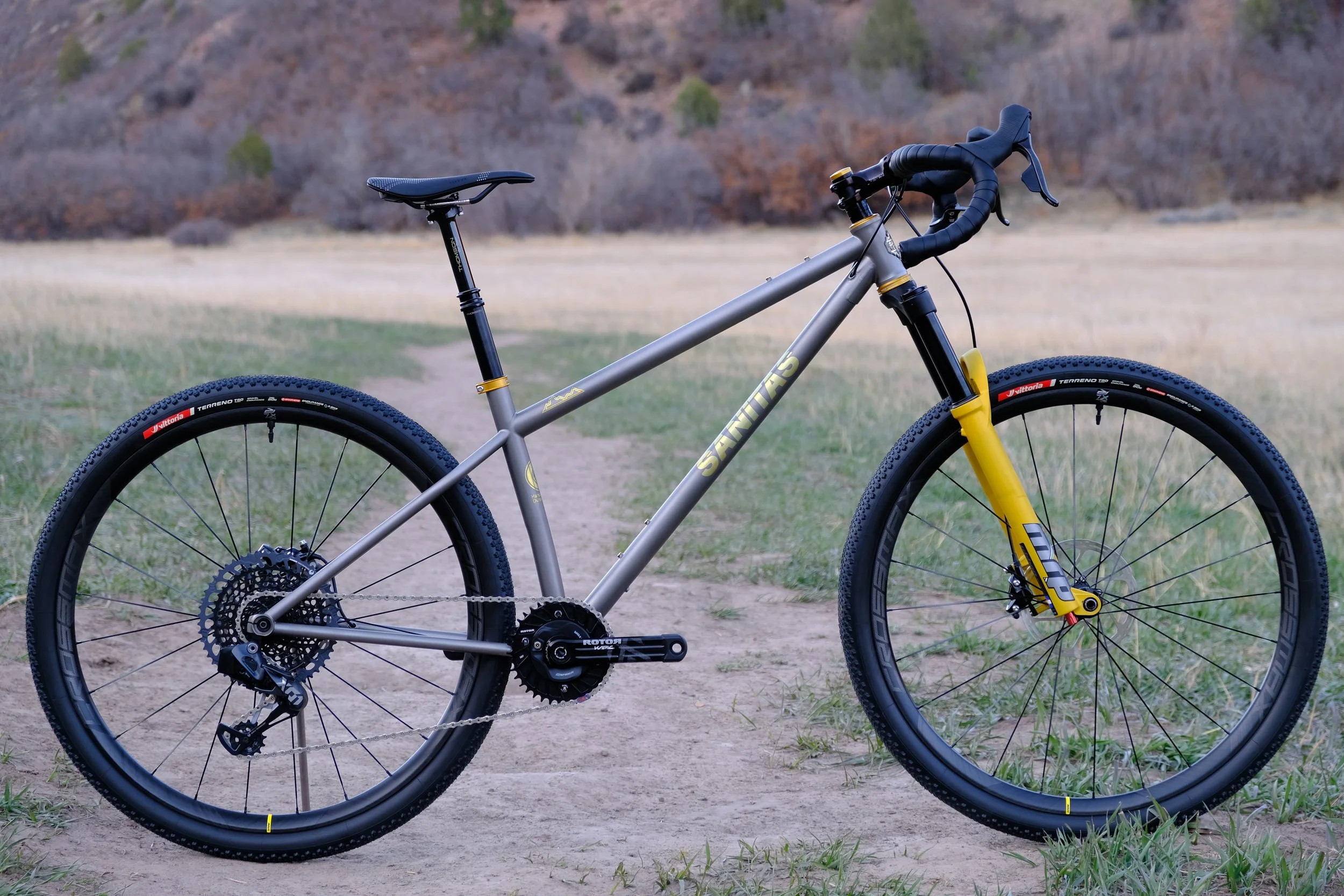 A gray and yellow mountain bike on a dirt trail in a natural outdoor setting with grass and trees in the background.