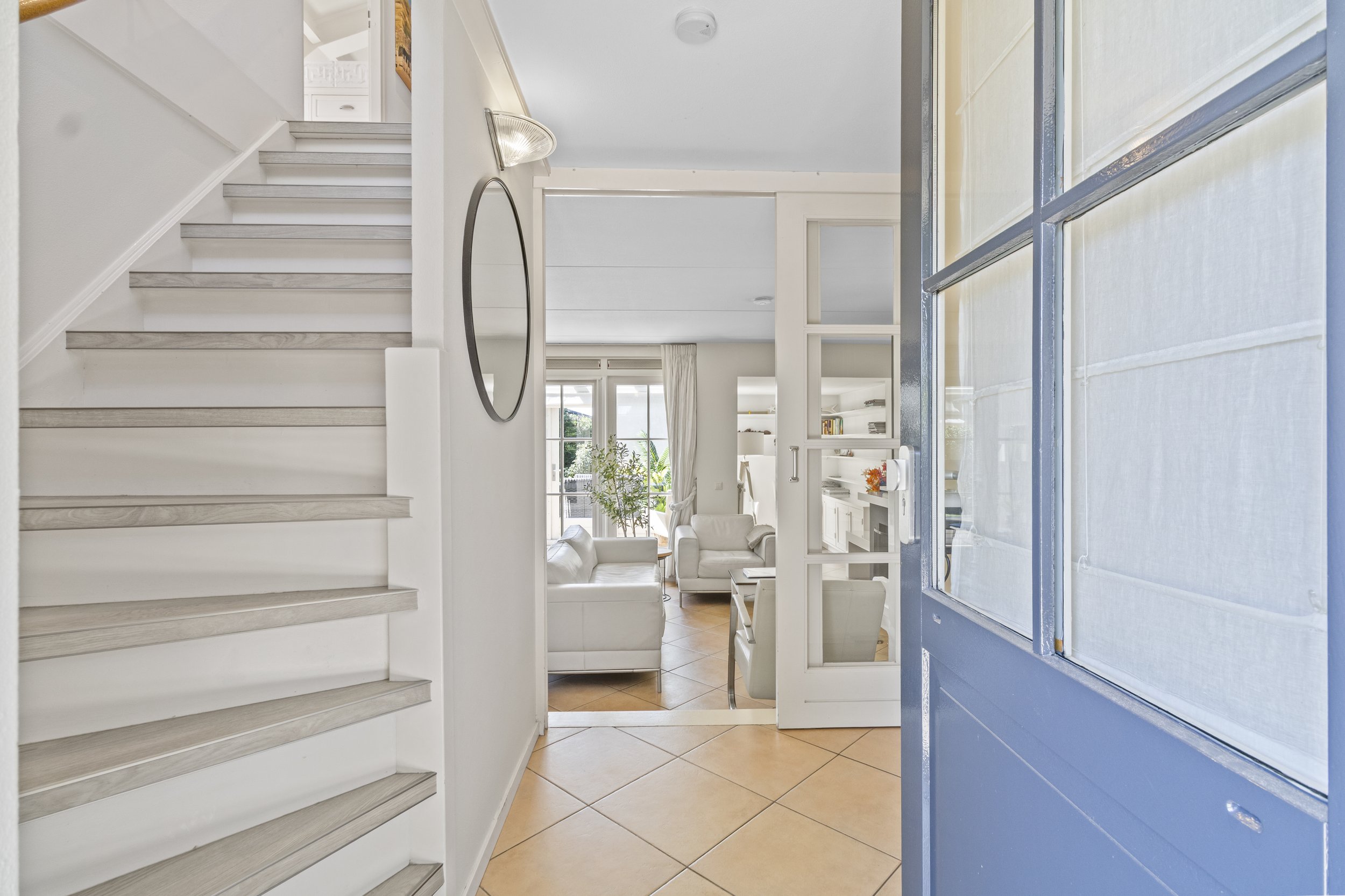 Ingang van een wit interieur huis met uitzicht op een woonkamer met witte banken en veel natuurlijk licht.