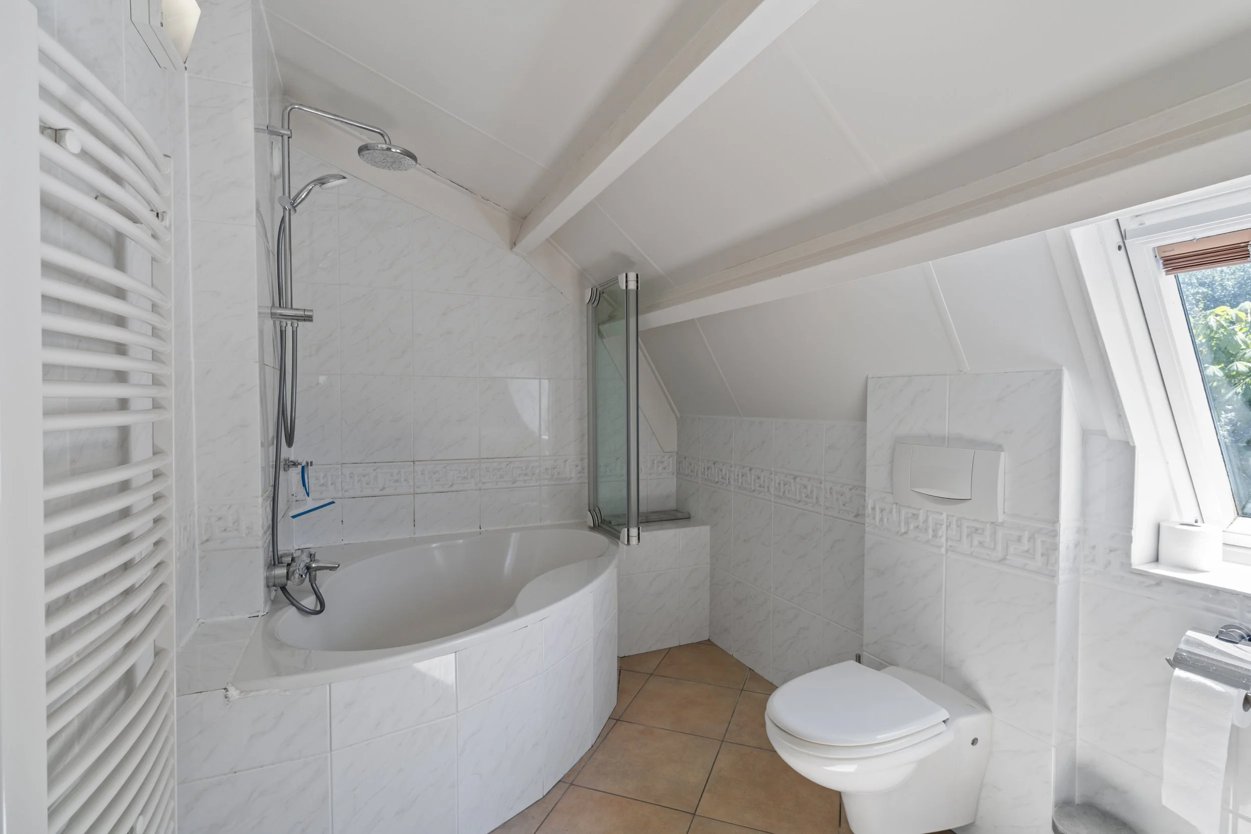 Badkamer met hoekbad, toilet en een venster met uitzicht op groen buiten.