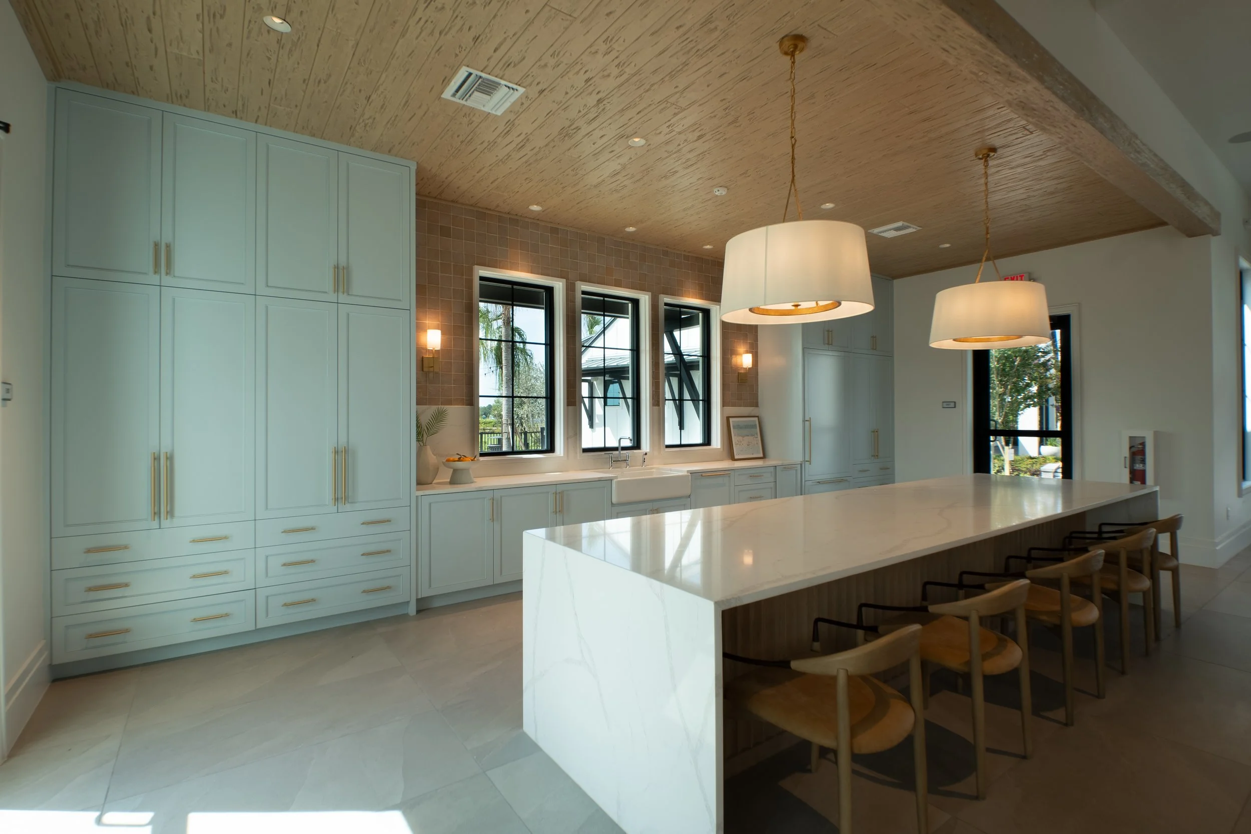 Modern kitchen with white cabinetry, a large marble island, pendant lights, and three large windows letting in natural light.