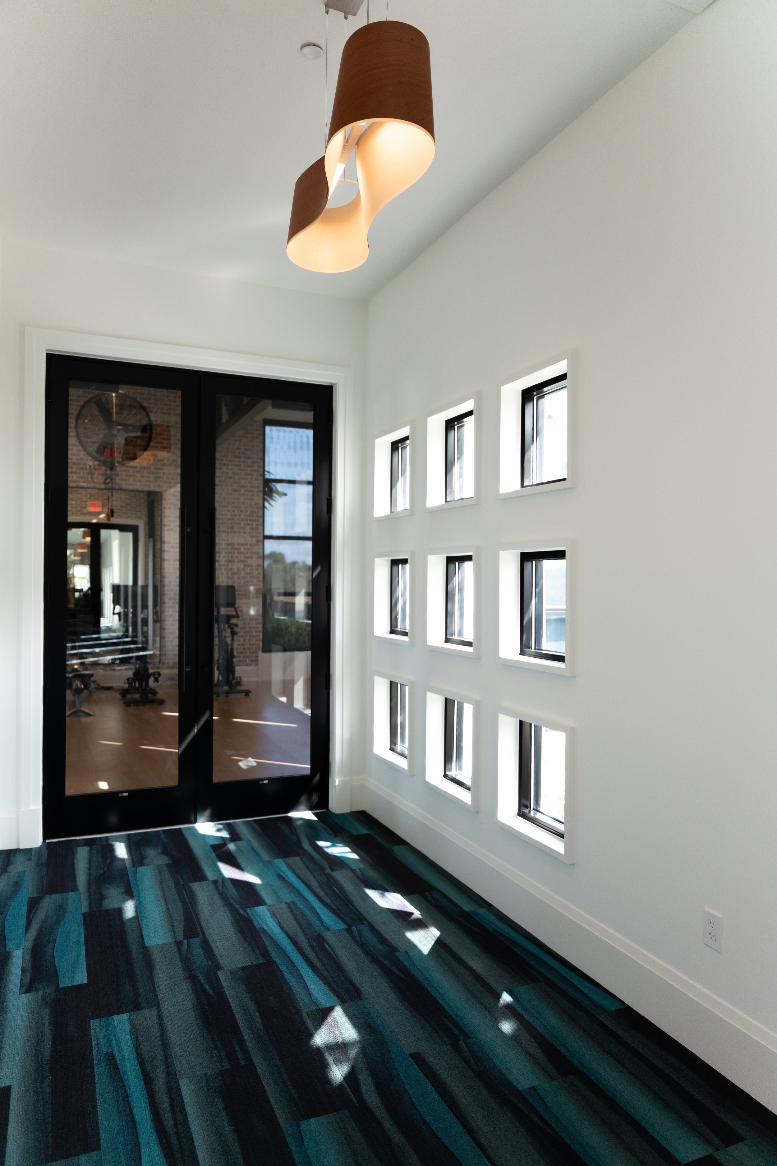 Interior view of a modern building with white walls, small square windows, a colorful striped carpet, and a ceiling light fixture.