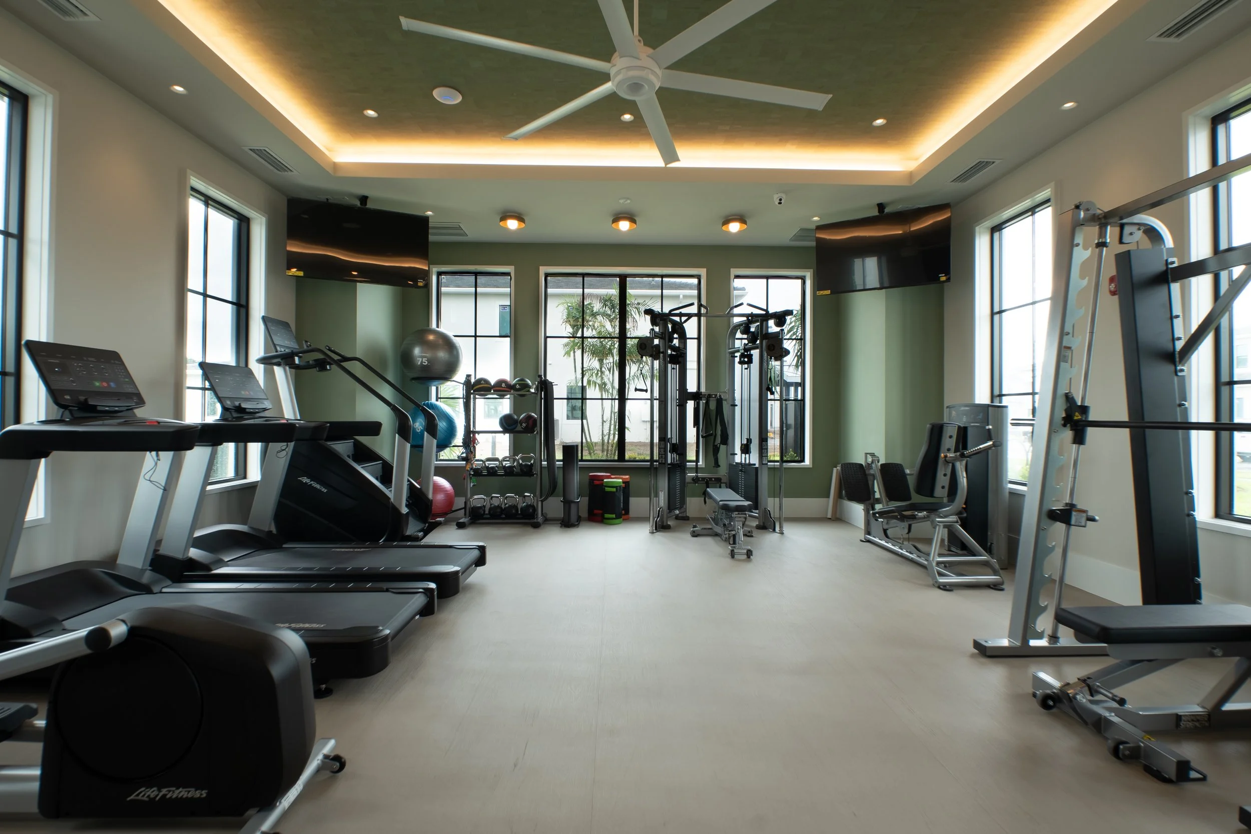 A modern gym with treadmills, strength training equipment, exercise balls, and large windows letting in natural light.